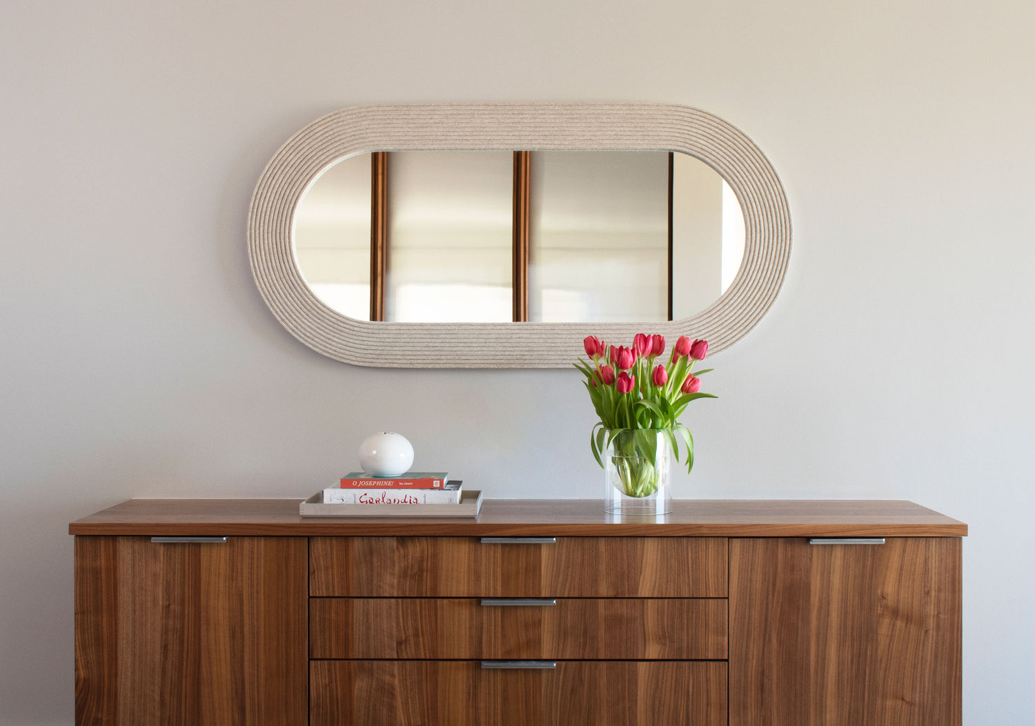 a long rectangular felt wall art with vertical lines in various shades of purple hangs over a MCM style bright green chair and a small table with a snake plant.