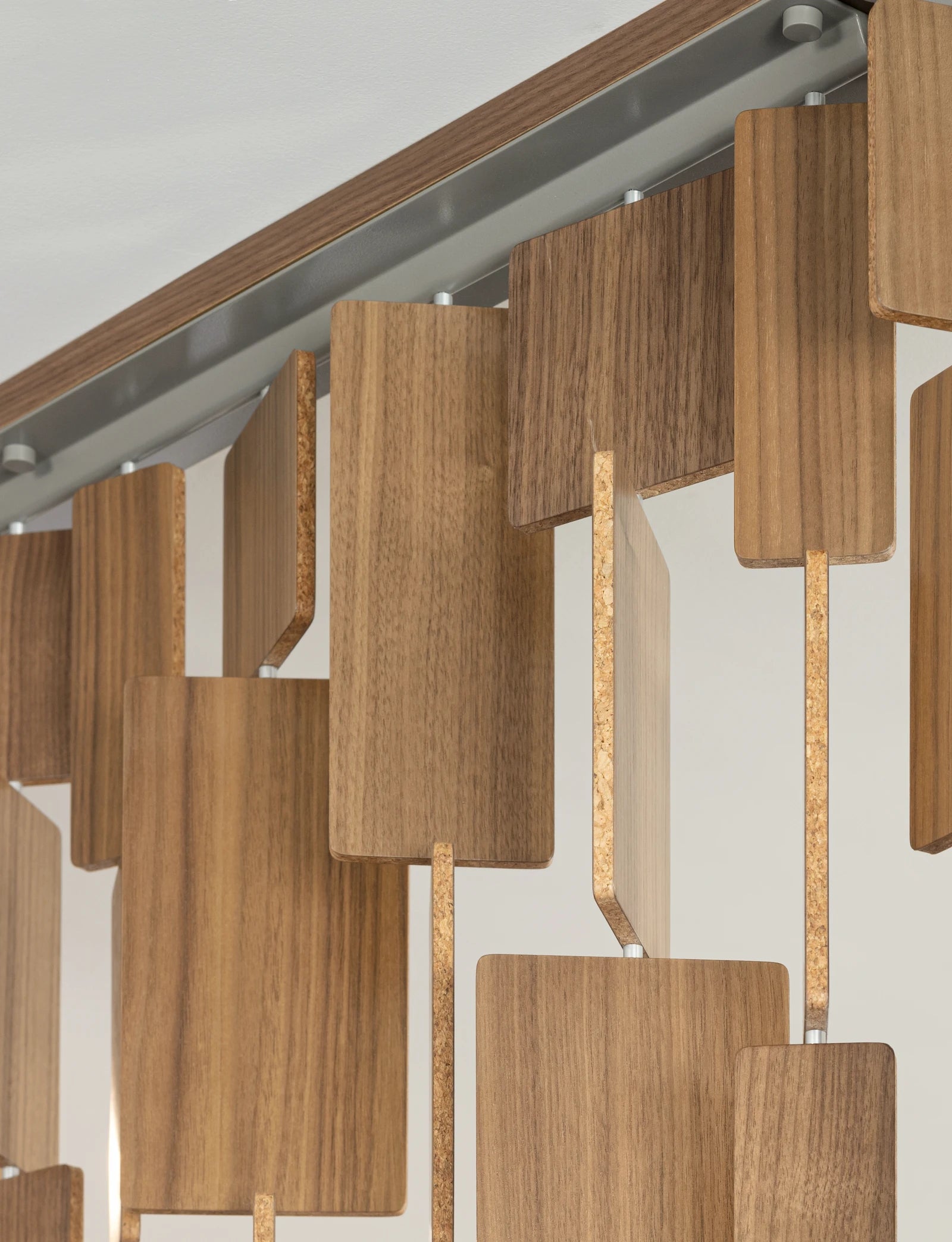 The powder-coated metal hanging hardware for the Century Screen. From the ceiling mount hangs tiles of various lengths made from walnut veneer with a cork core.