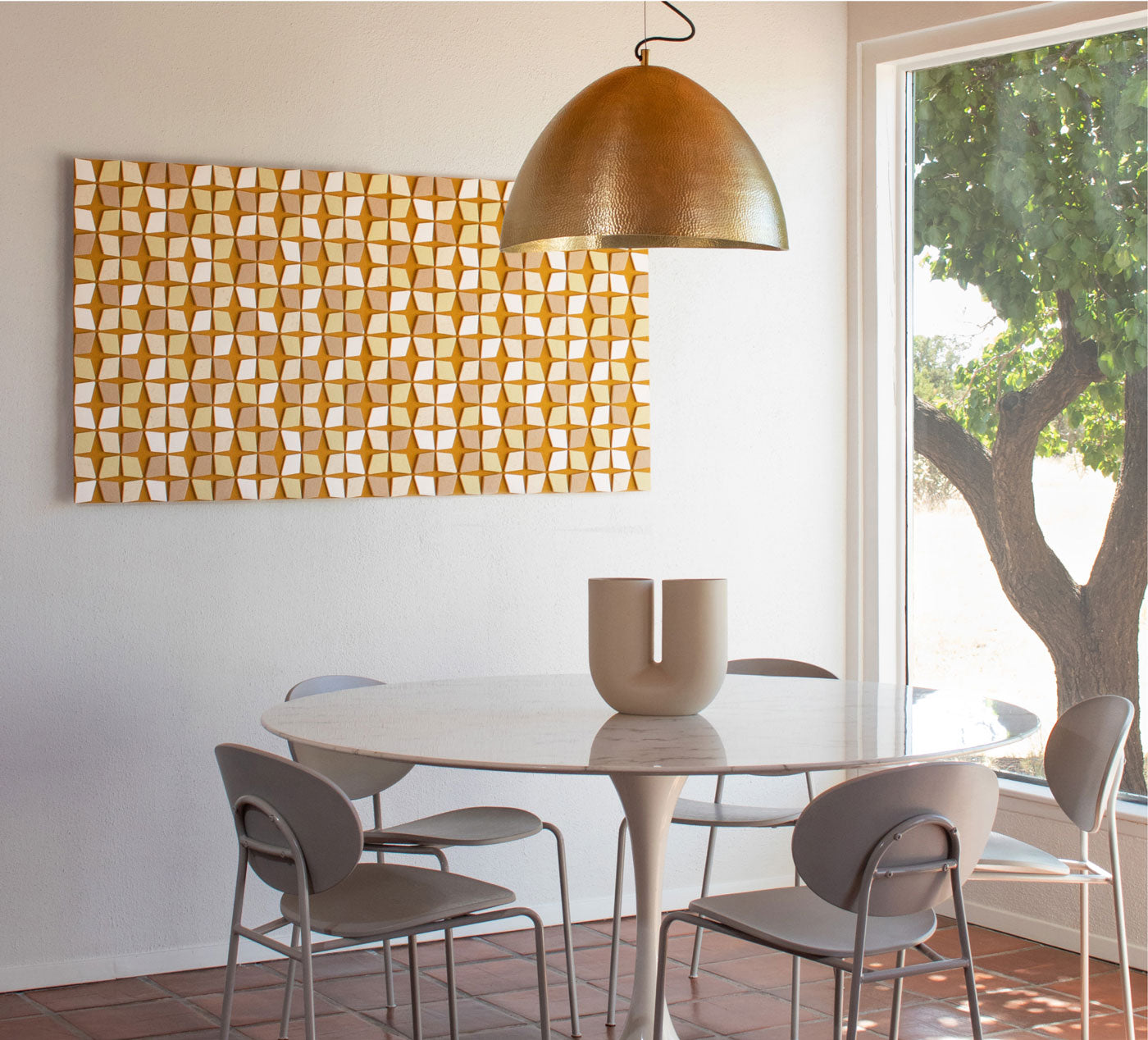 Dining room with a round table and chairs, gold pendant light, and abstract felt art on the wall.