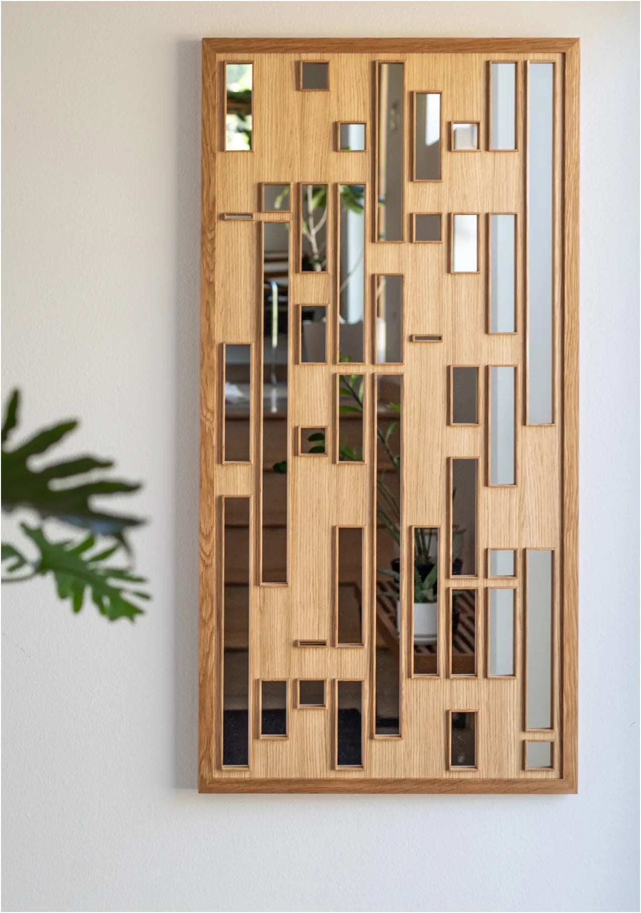 A rectangle mirror hangs on a white wall The mirror has a white oak frame and the reflective glass can only be seen below various square and rectangle framed cutout on the surface.