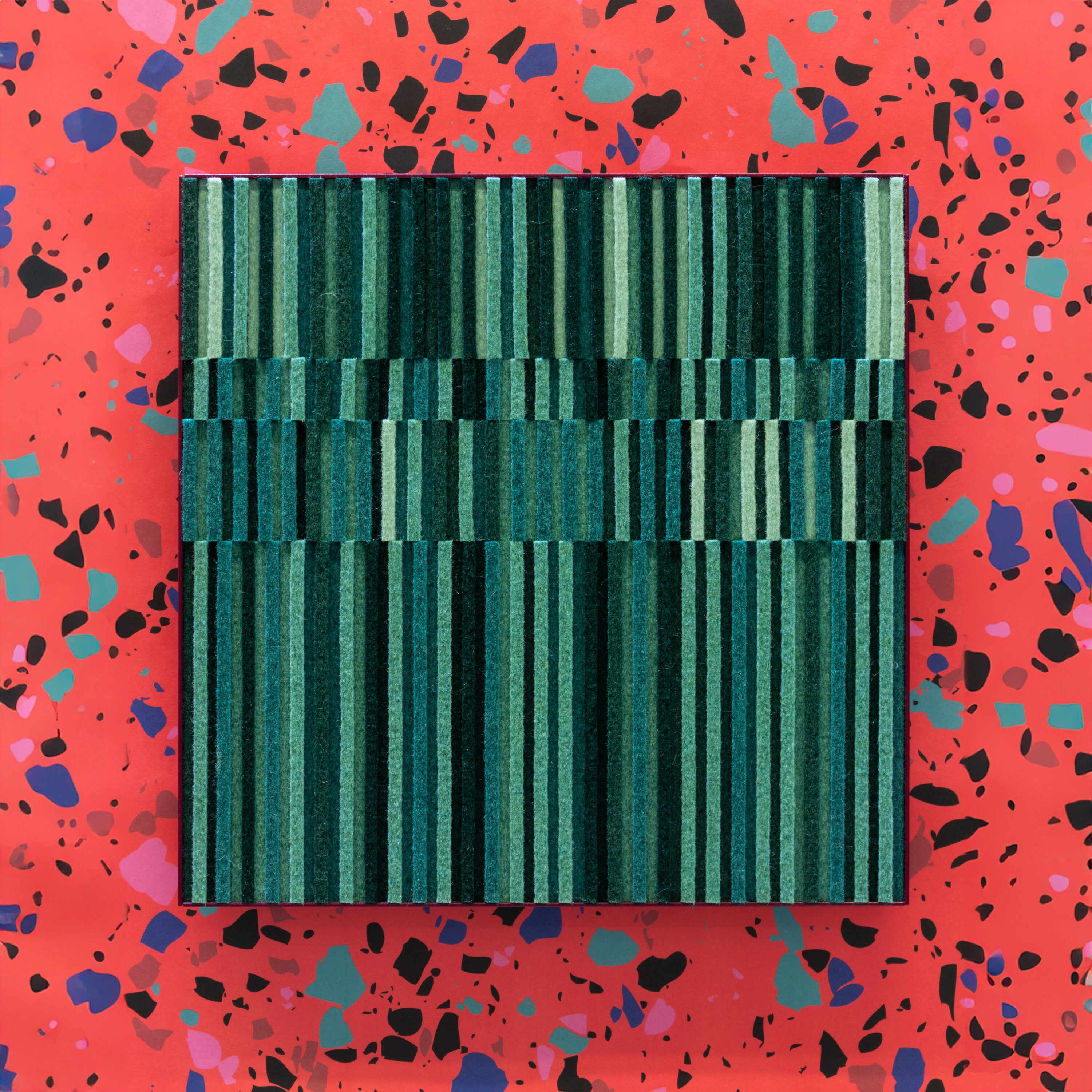 A small wall art piece of rows of alternating height felt in various tones of green in a violet colored metal cradle. Circadian No. 2 is hung here on a wallpaper of pink, black, and blue terrazzo. #color_Multi-Green
