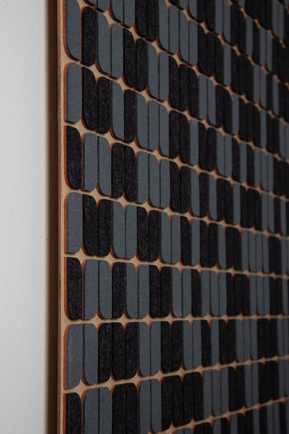 A felt wall panel seen from the side The background is a tan wool felt with gray and gray-blue rounded shapes on the surface and a slight pop of orange felt seen from the side.