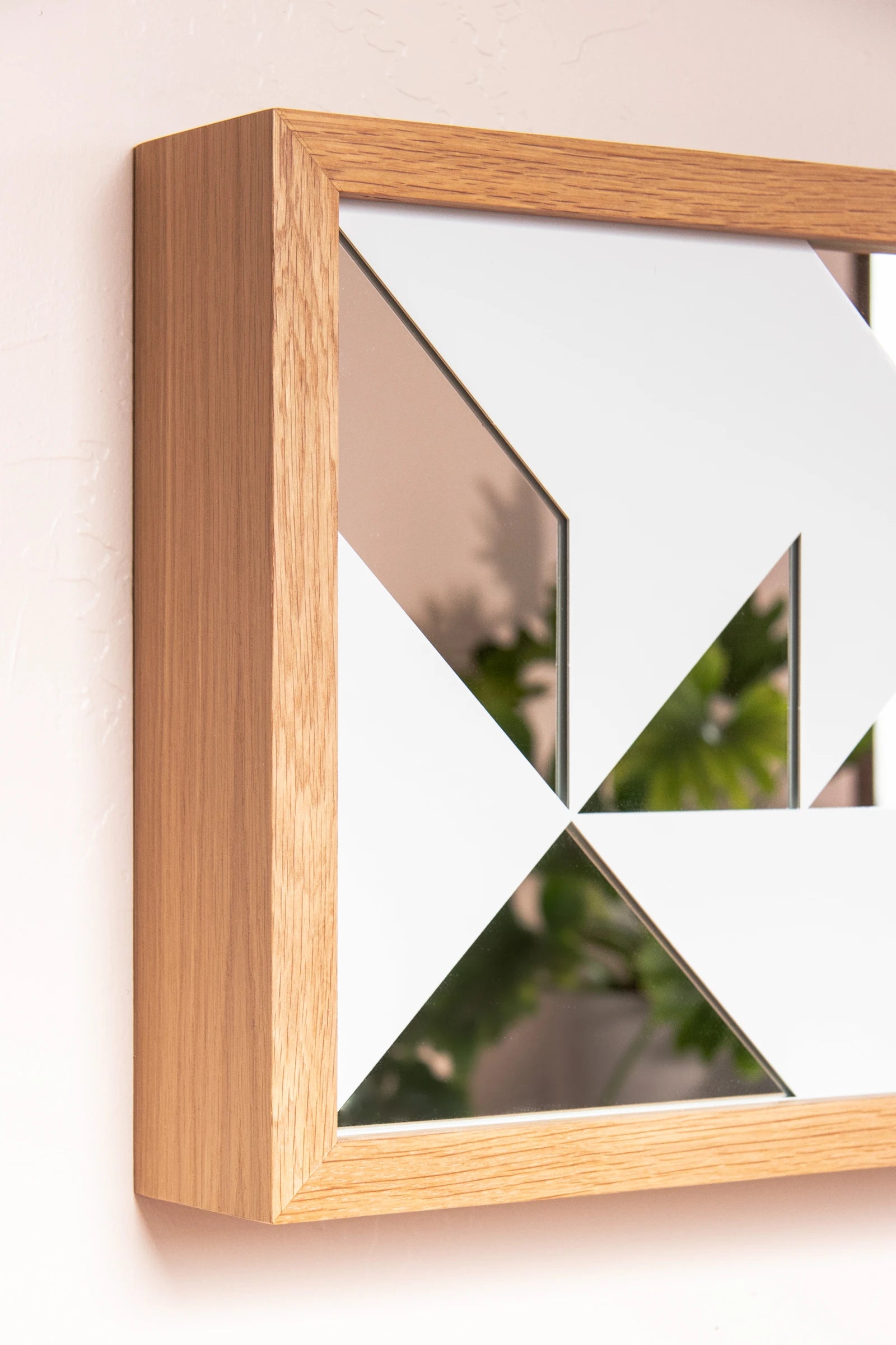 A deep wooden frame holds a reflective surface covered partially by a white metal lattice with geometric shapes.