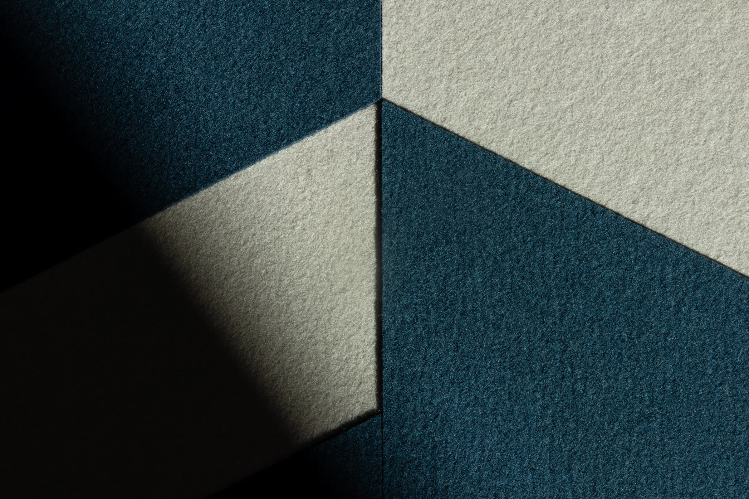 A close up of a two tone felt wall art piece with both bright light and shadow. It has tan and dark blue felt in geometric shapes