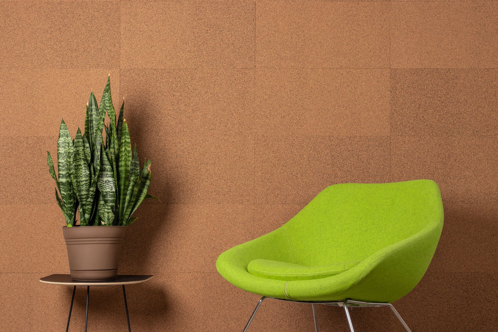 Green modern chair and potted plant against a tan and black textured cork wall
