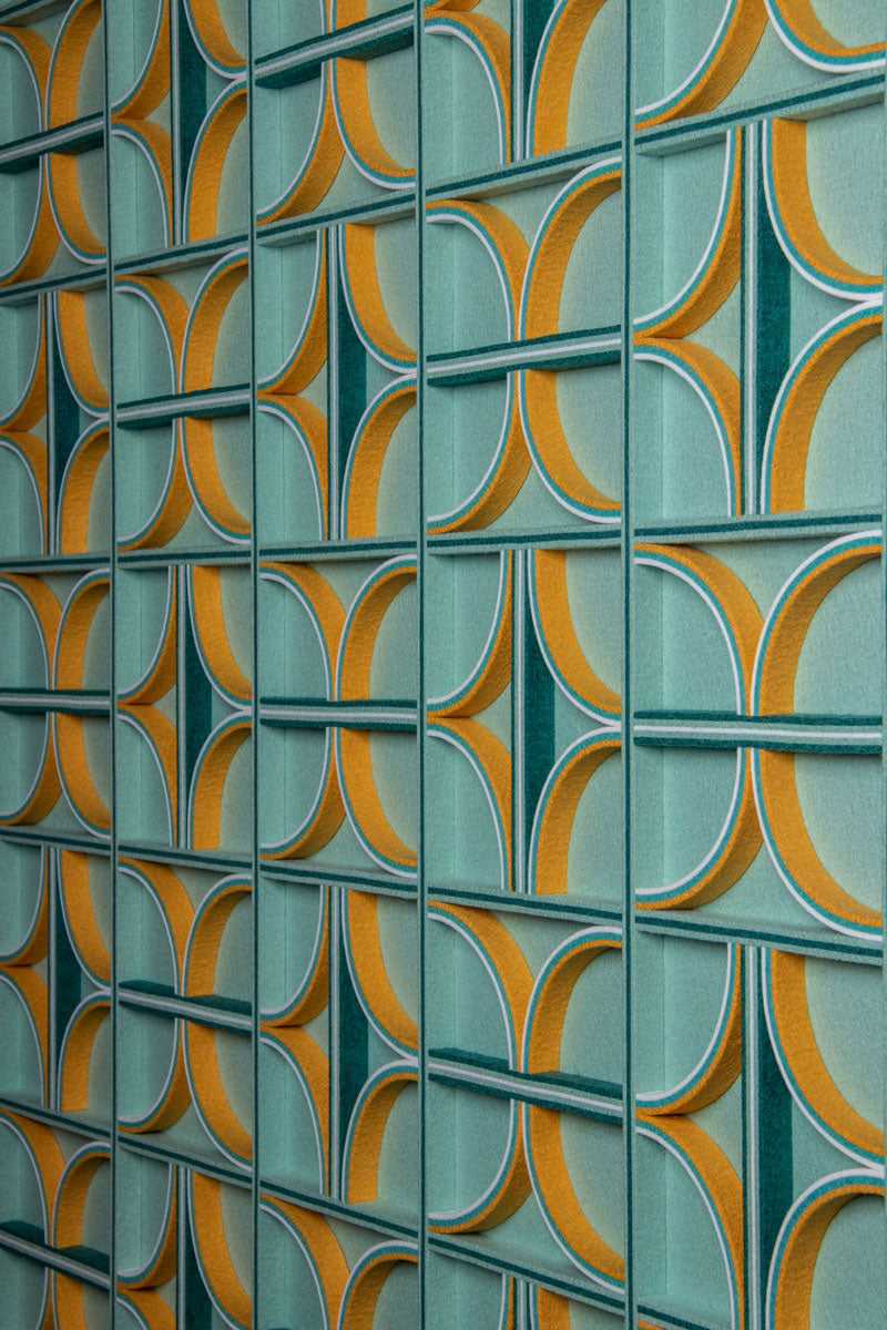 Patterned felt wall art with curved and straight felt details on edge. The background is a teal or sage color, and the details are yellow, white, teal, and dark green.