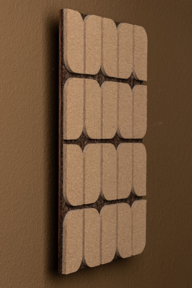 A flat wall panel with a geometric pattern consisting of curved-edge rectangular shapes, with a dark smoked cork background and tan felt details. Hung at an angle on a medium brown wall.