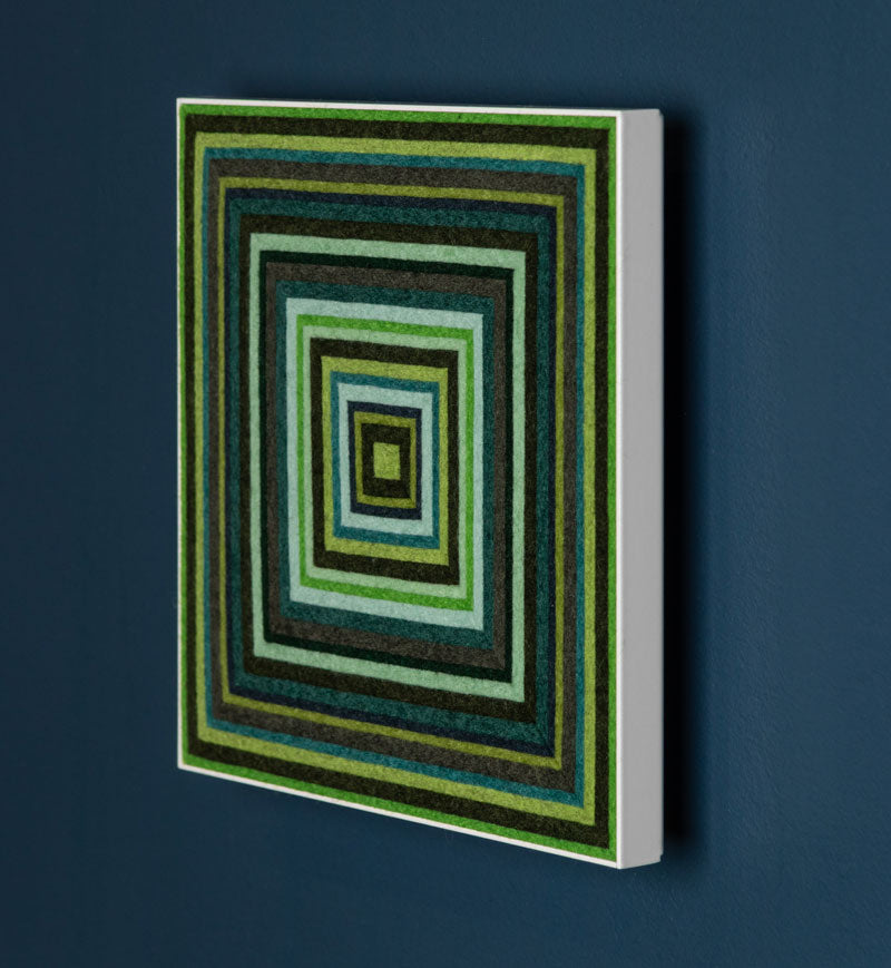 A rectangular panel with a geometric pattern of concentric squares in various shades of green and blue seen from the side on a blue wall.