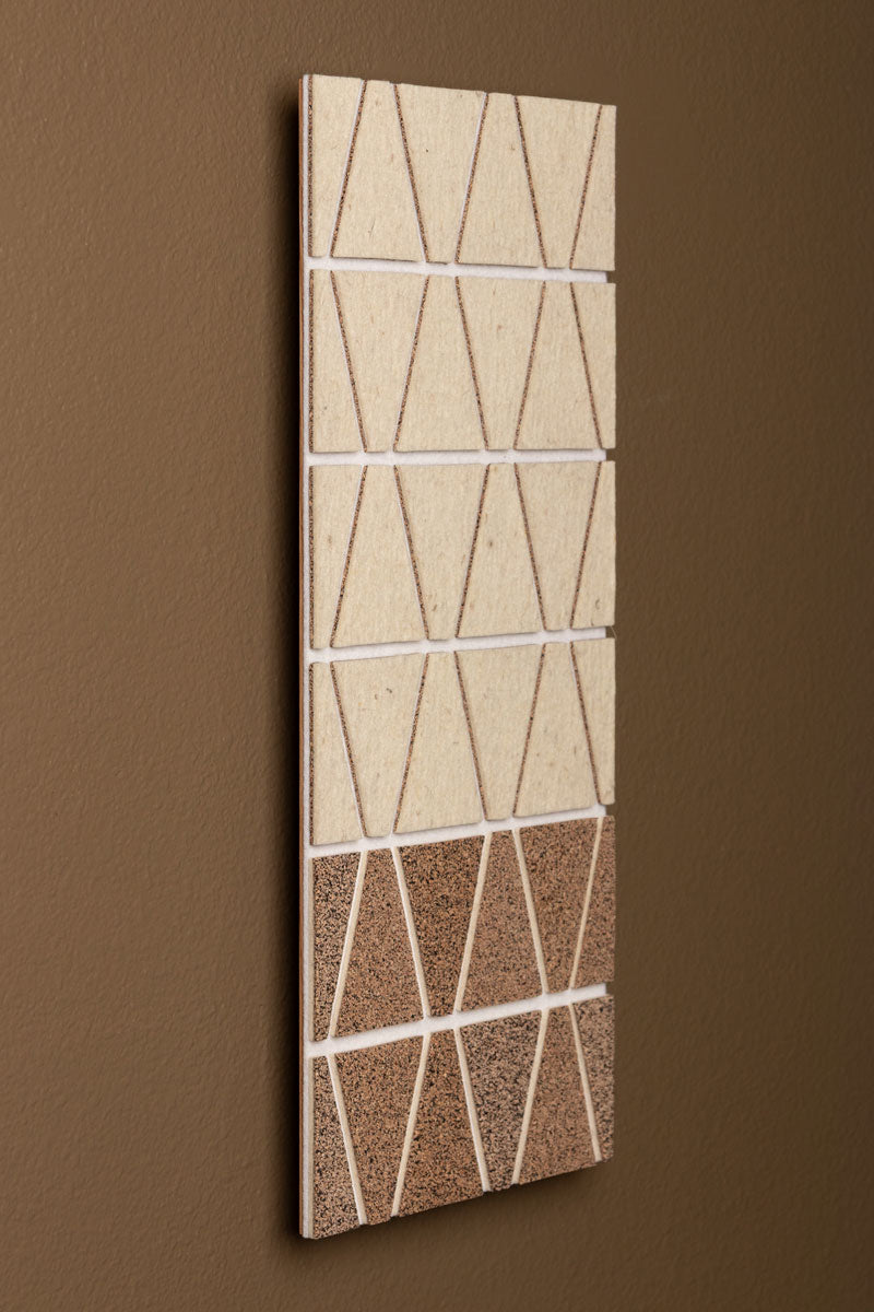 A long rectangular wall art panel featuring a geometric pattern with trapezoid shapes in beige felt and brown speckled cork on a brown wall seen from the side.