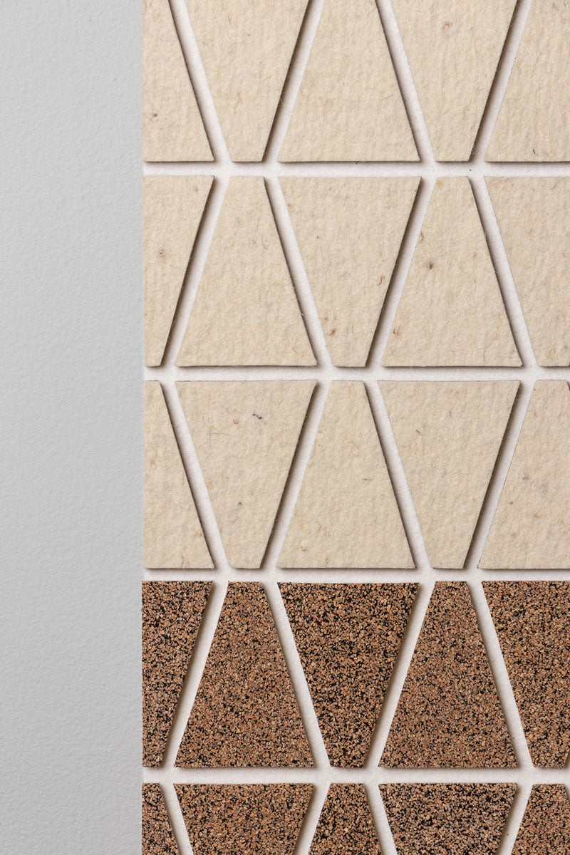 Close up of the edge of a wall art panel featuring a geometric pattern with trapezoid shapes in beige felt and brown speckled cork on a white wall.