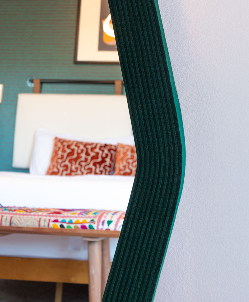 The edge of a dark green felt edged mirror reflecting a bedroom