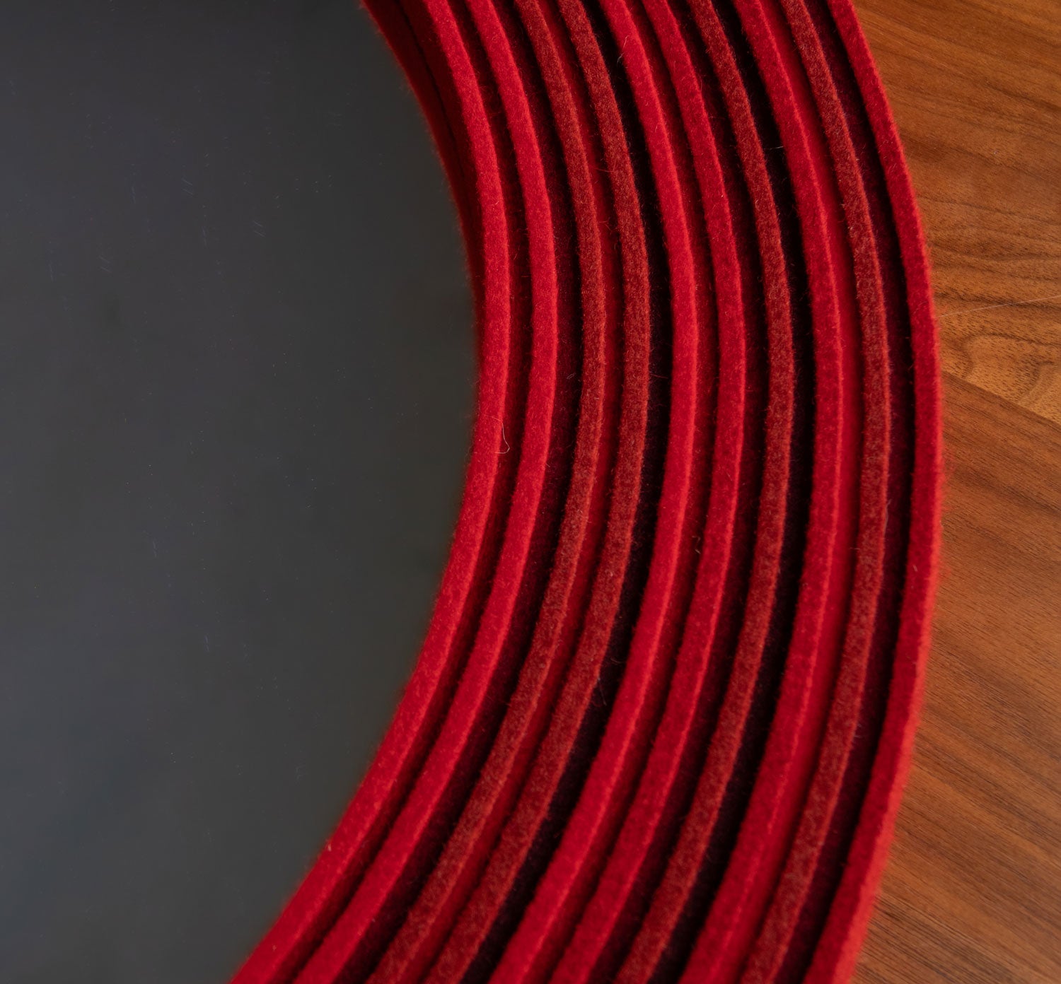 Close up of the felt frame of a mirror. The felt is on edge in alternating heights in tones of red.