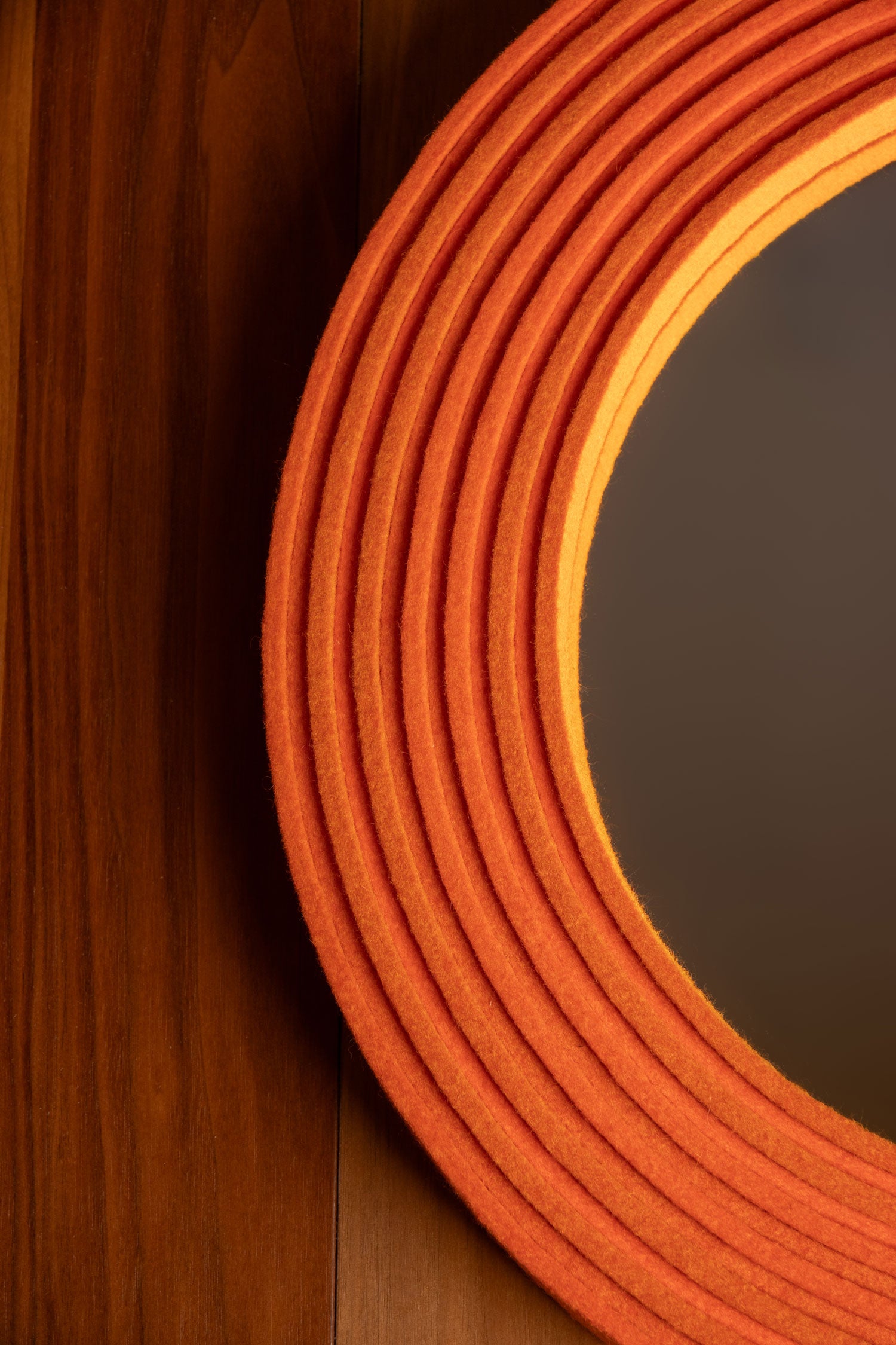 A closeup of a round mirror with a felt frame. The frame is on edge felt laid out in alternating heights of orange felt.