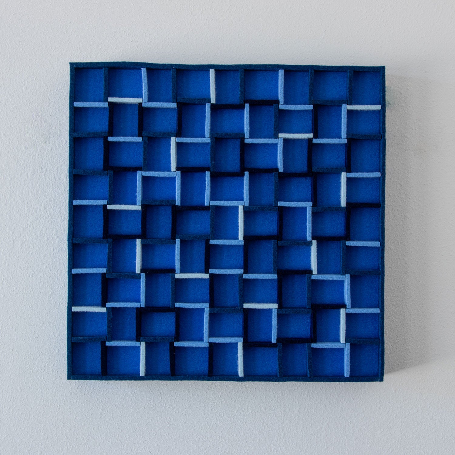 A square blue geometric wall art piece with a 3D layered cube pattern, mounted on a light gray textured wall. #color_Multi blue