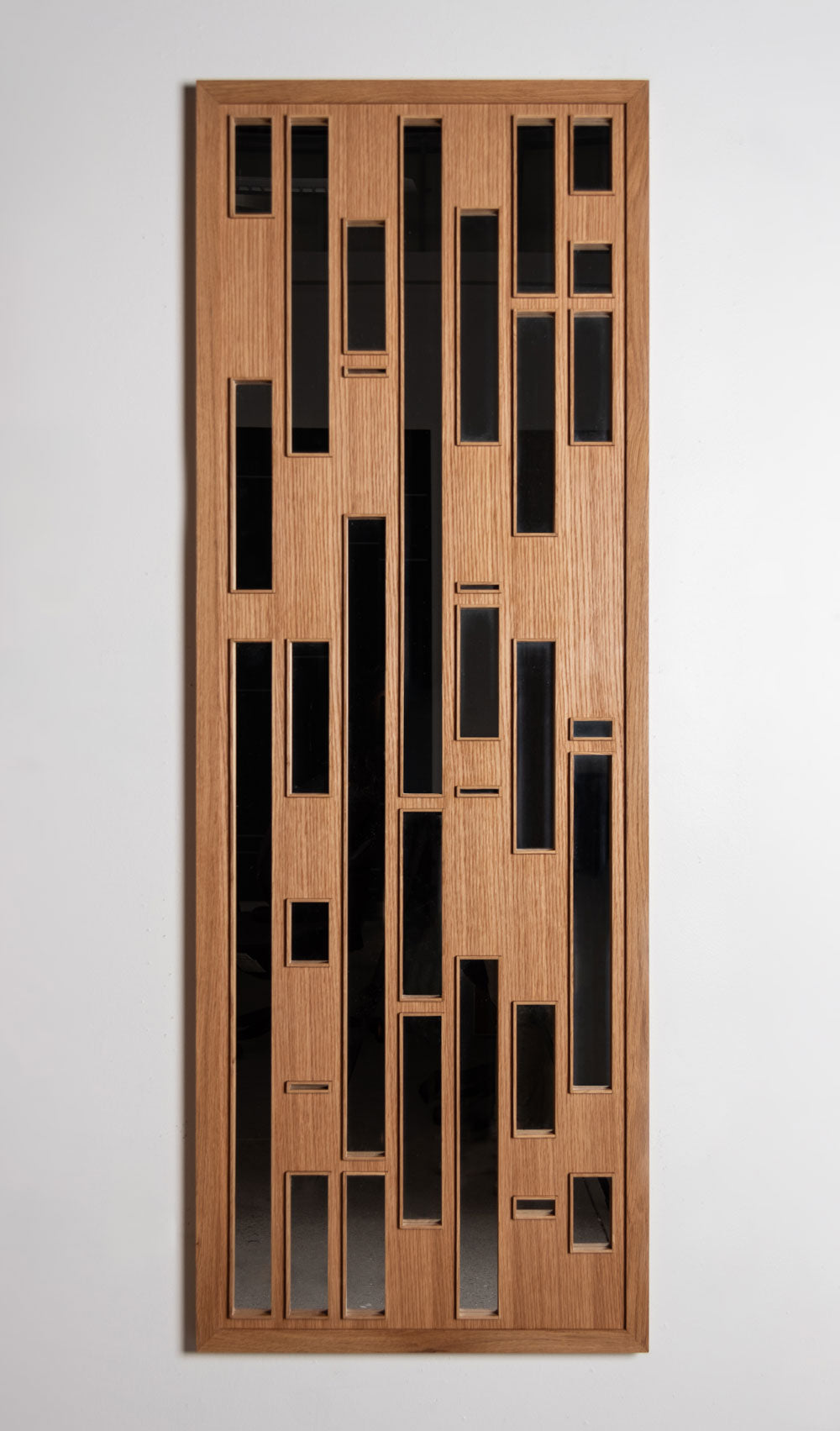 A tall rectangular wood mirror with long vertical apertures on a white wall.