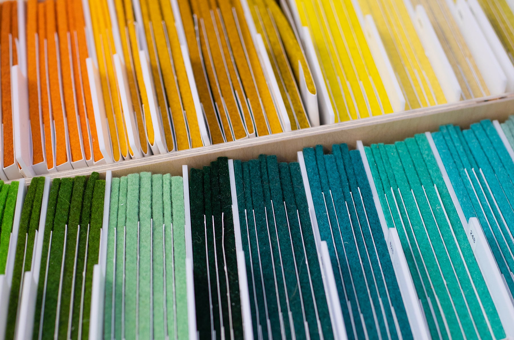 Drawers full of wool felt samples. On the bottom is tones of green and blue, and above it is tones of orange and yellow.