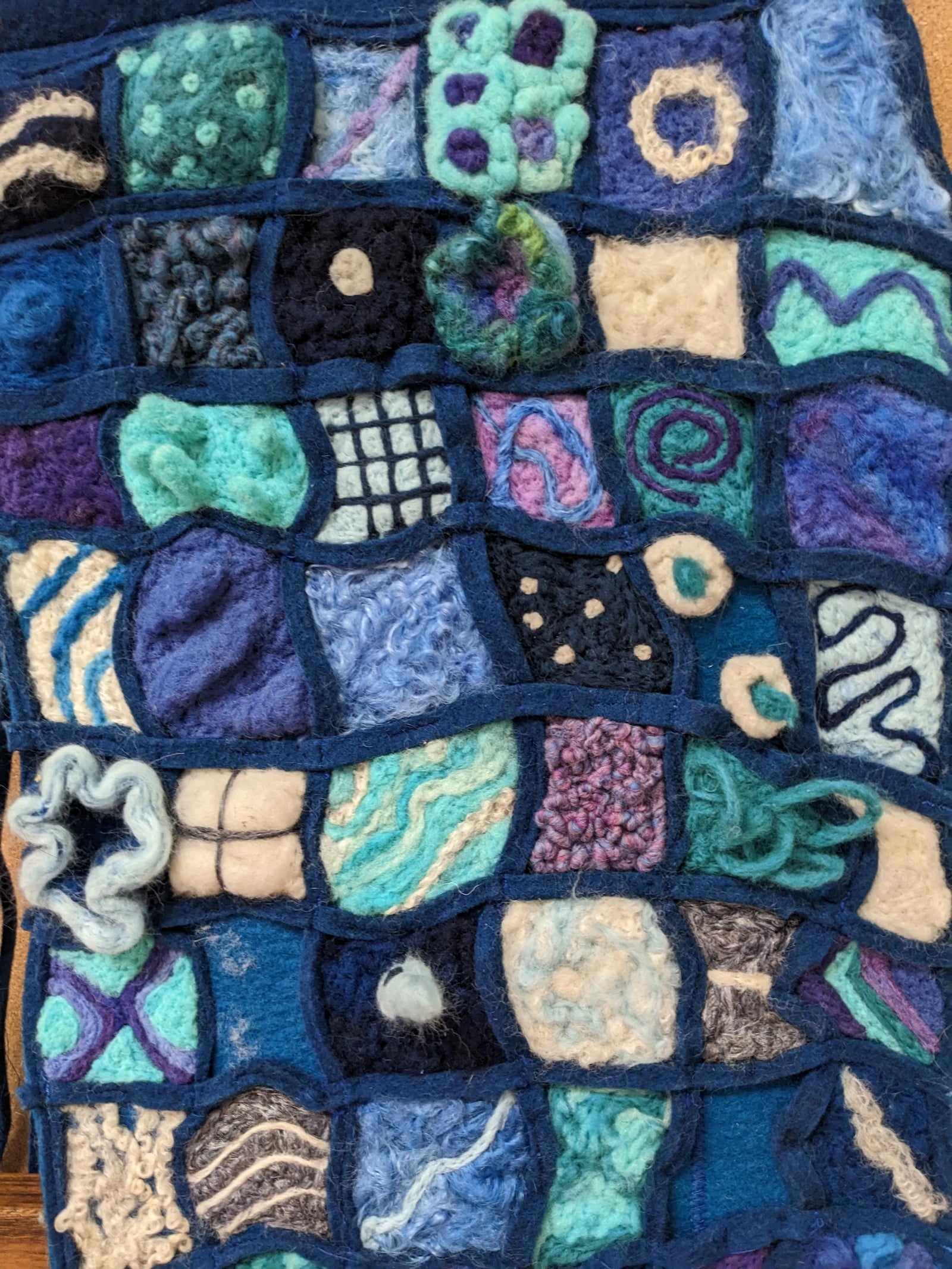 A quilt-like textile made with various threads and yarn and a framing of blue felt