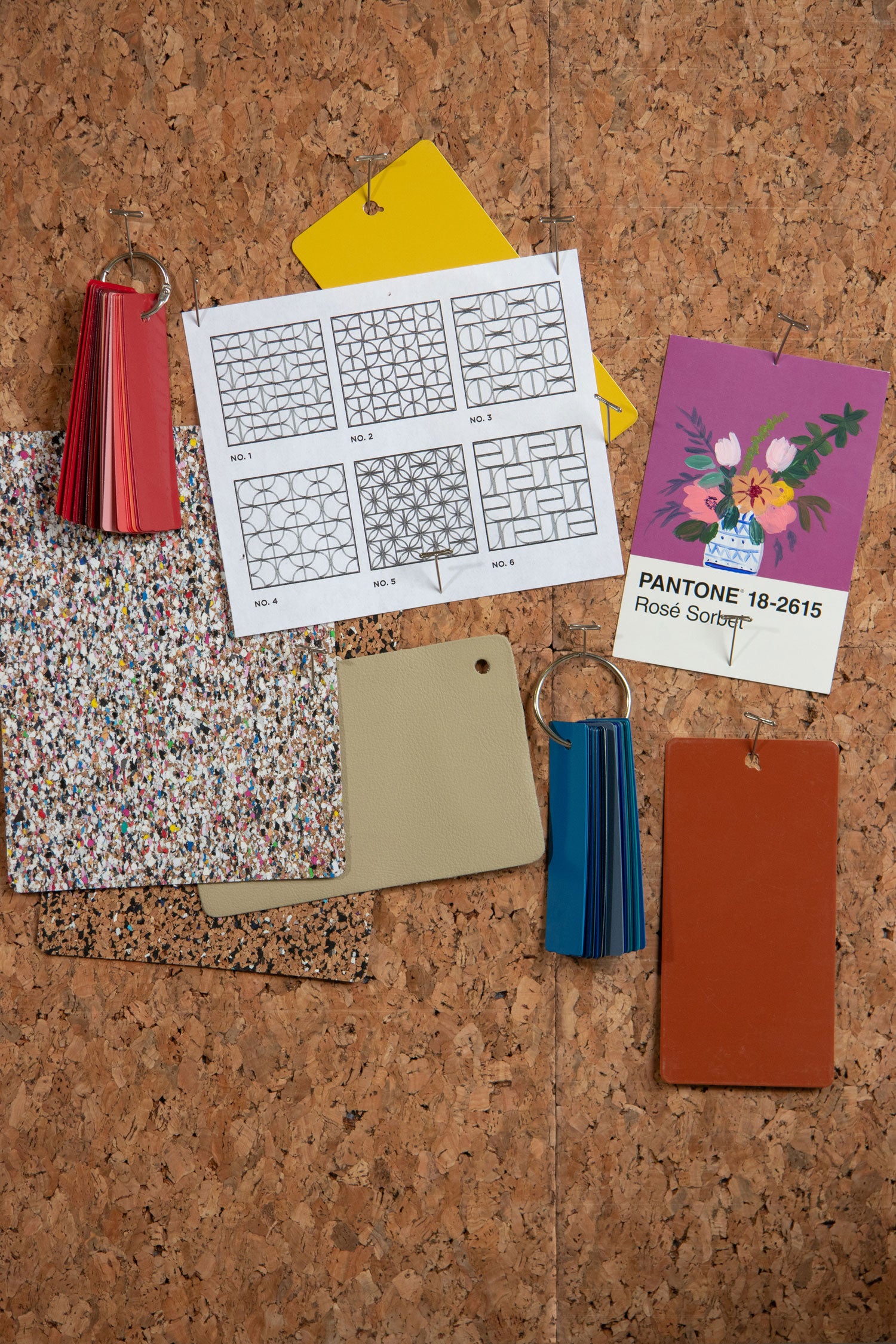 Collection of color swatches, cards, and a pattern sheet on a corkboard.