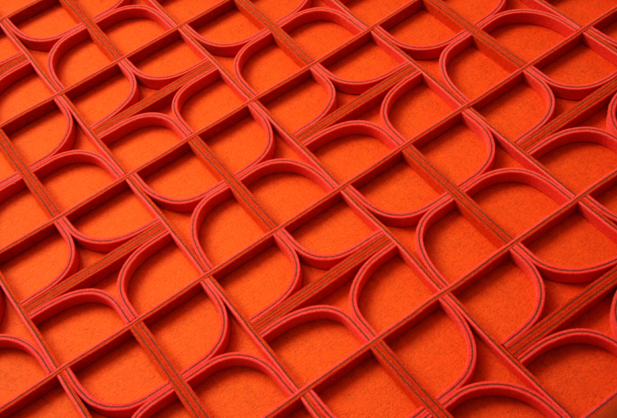 A felt wall panel seen from the side. The background is an orange felt and the dimensional pattern is created with straight lines and quarter circles of red and purple felt on edge.