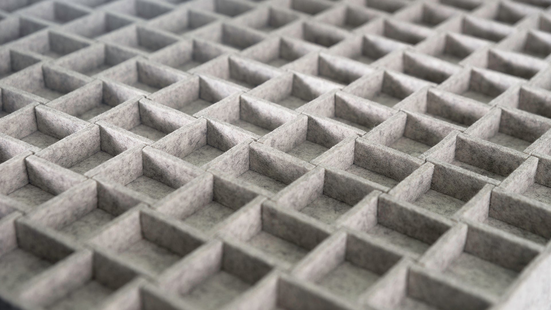 A closeup of a gray felt wall panel with uniform square shaped formed from felt on edge.