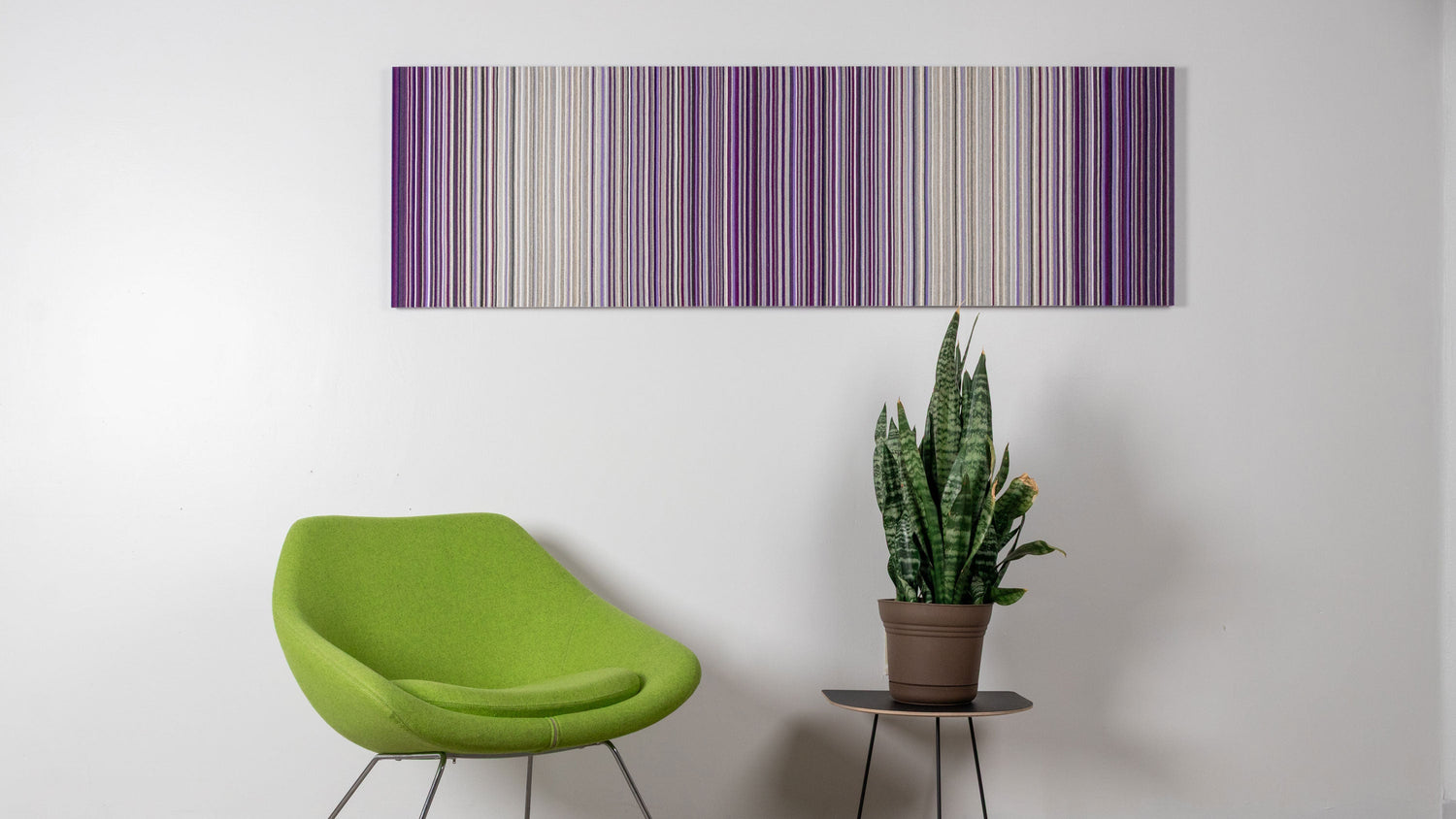 A long rectangular purple and white felt wall art  hangs over a bright green chair