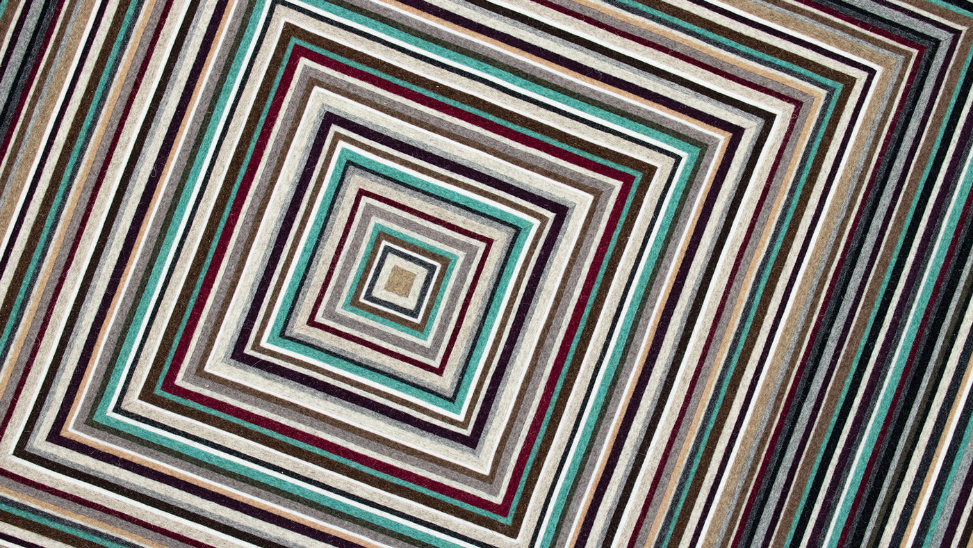a closeup of concentric squares of strips of wool felt in neutrals with a pop of red and turquoise. 