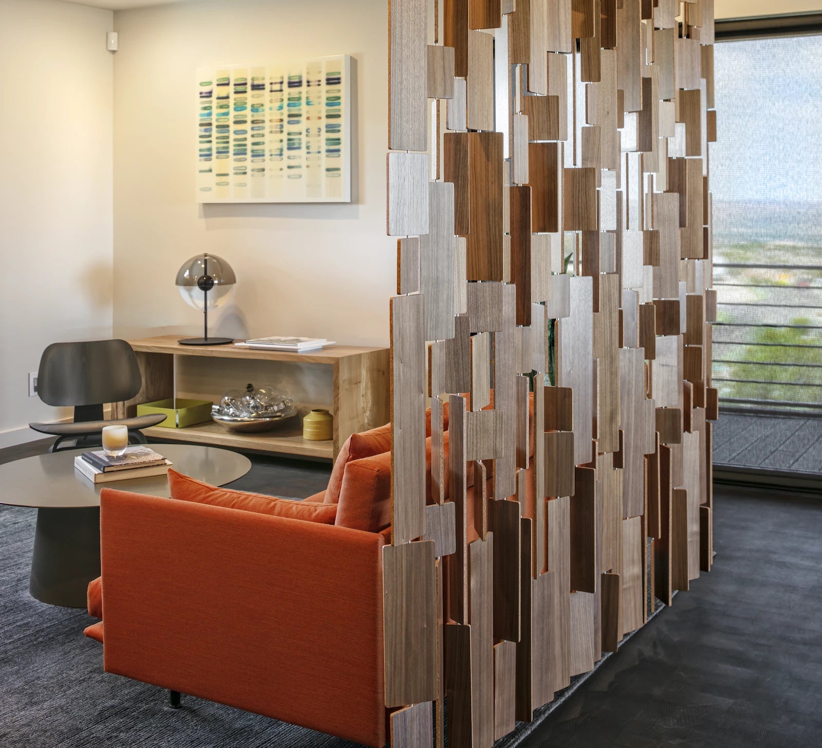 The Century Screen is tiles of walnut veneer with a core center hung in various lengths from the ceiling. On the far side of the screen is a living room with modern furniture and decor. 