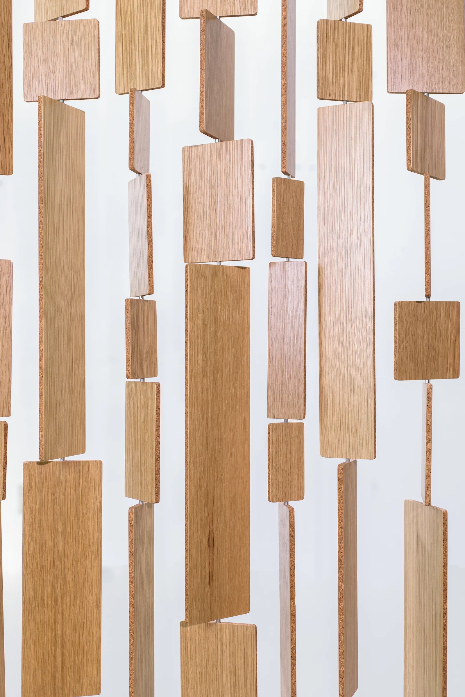 A close up of Century Screen which has tiles of white oak veneer with a core center hung in various lengths. Hanging in front of a white wall.