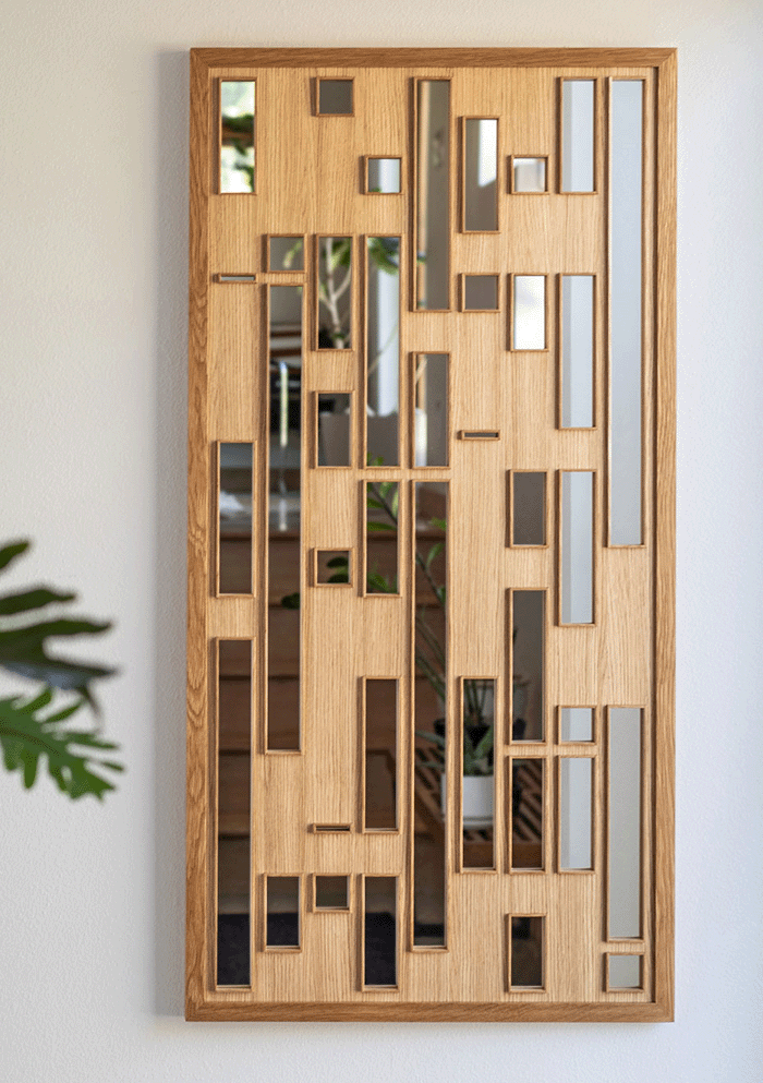 Wooden wall art piece with geometric design on a white wall, next to a plant.