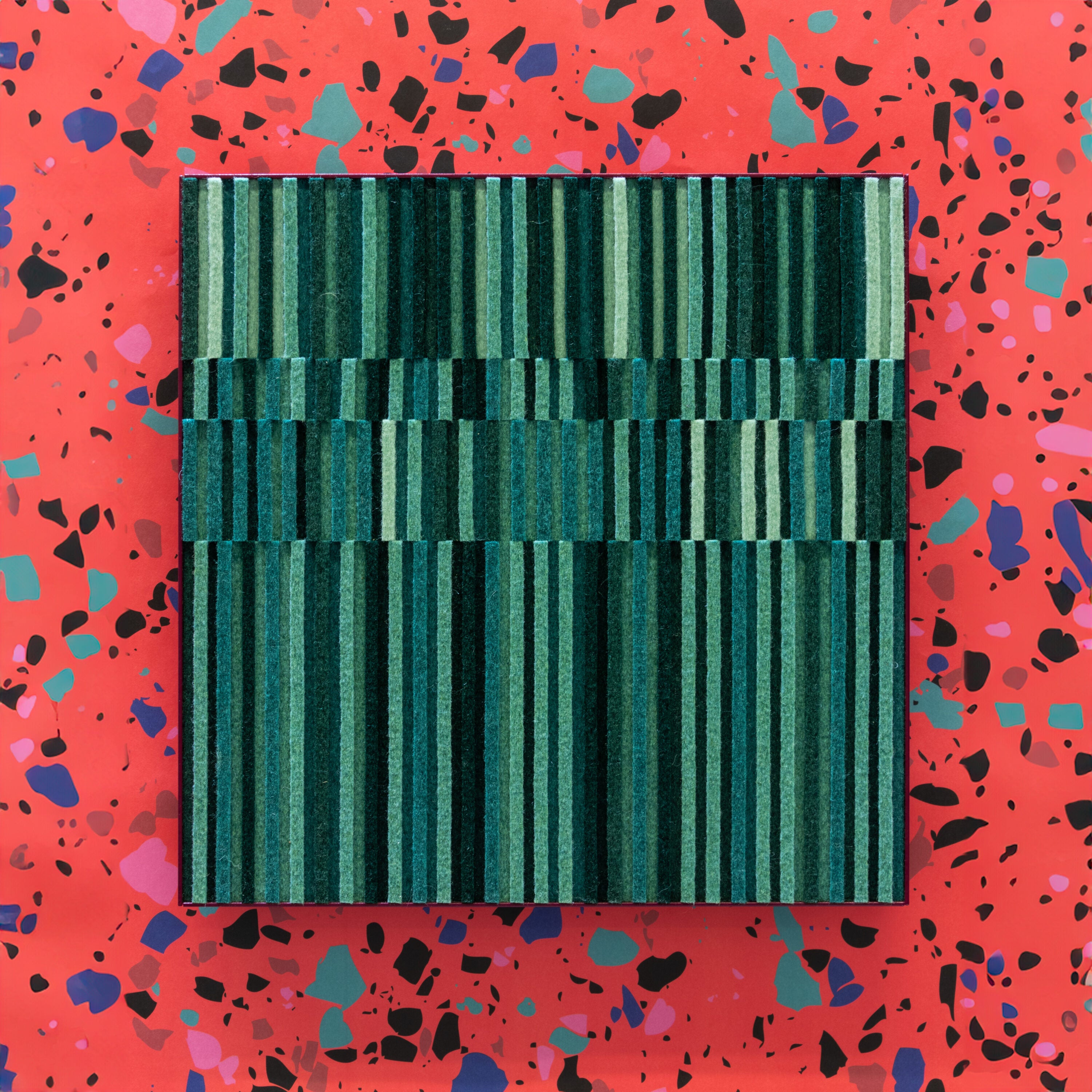 A small wall art piece of rows of alternating height felt in various tones of green in a violet colored metal cradle. Circadian No. 2 is hung here on a wallpaper of pink, black, and blue terrazzo. 