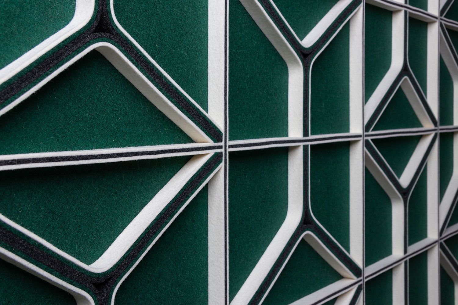 A large felt wall panel with a green face and green and white lines and angles seem closeup at an angle