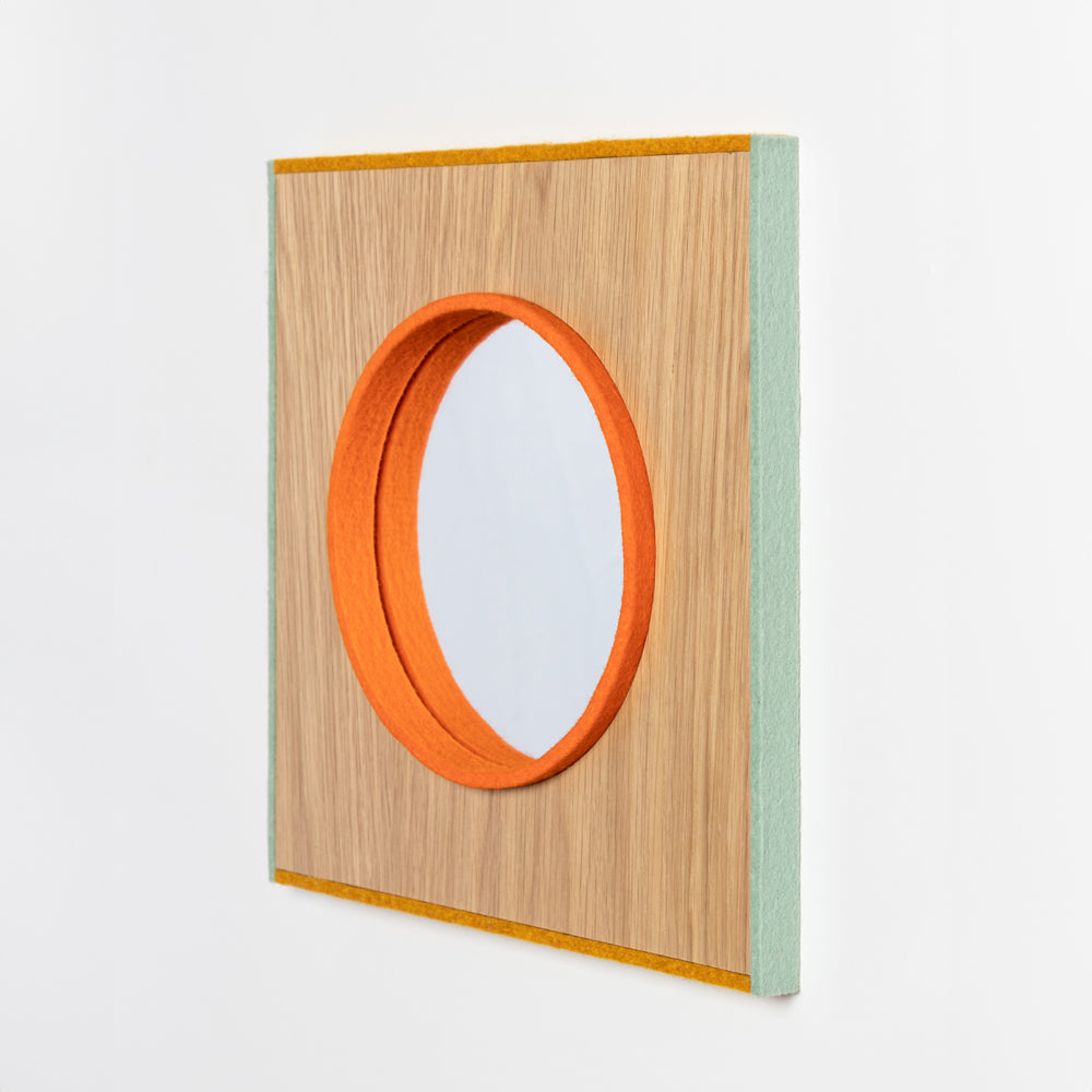 A small mirror framed with a strip of orange felt, surrounded by a wood surface and the whole thing framed with sage and yellow felt on the edges. 