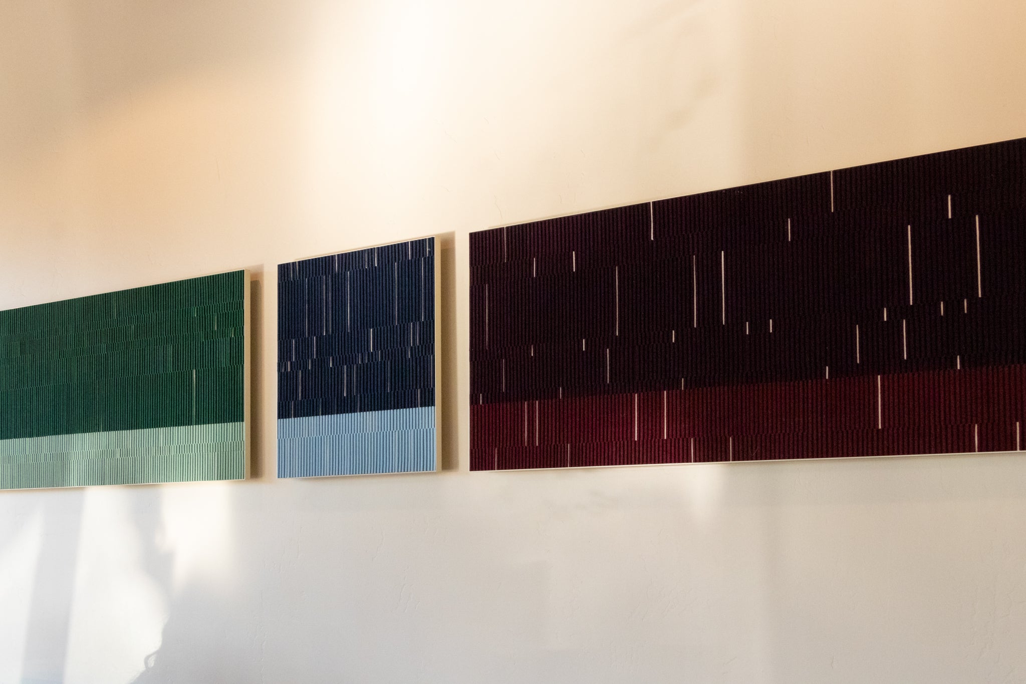 Three rectangular felt wall art panels, each with two tones of the same color and white vertical lines  throughout 