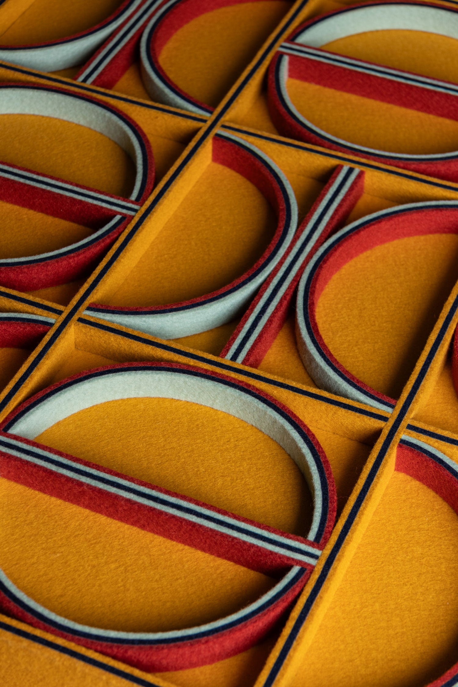 A felt surface with straight lines and half circles. The details are on-edge felt in colros of light and dark blue and red, and the surface is a mustard yellow.