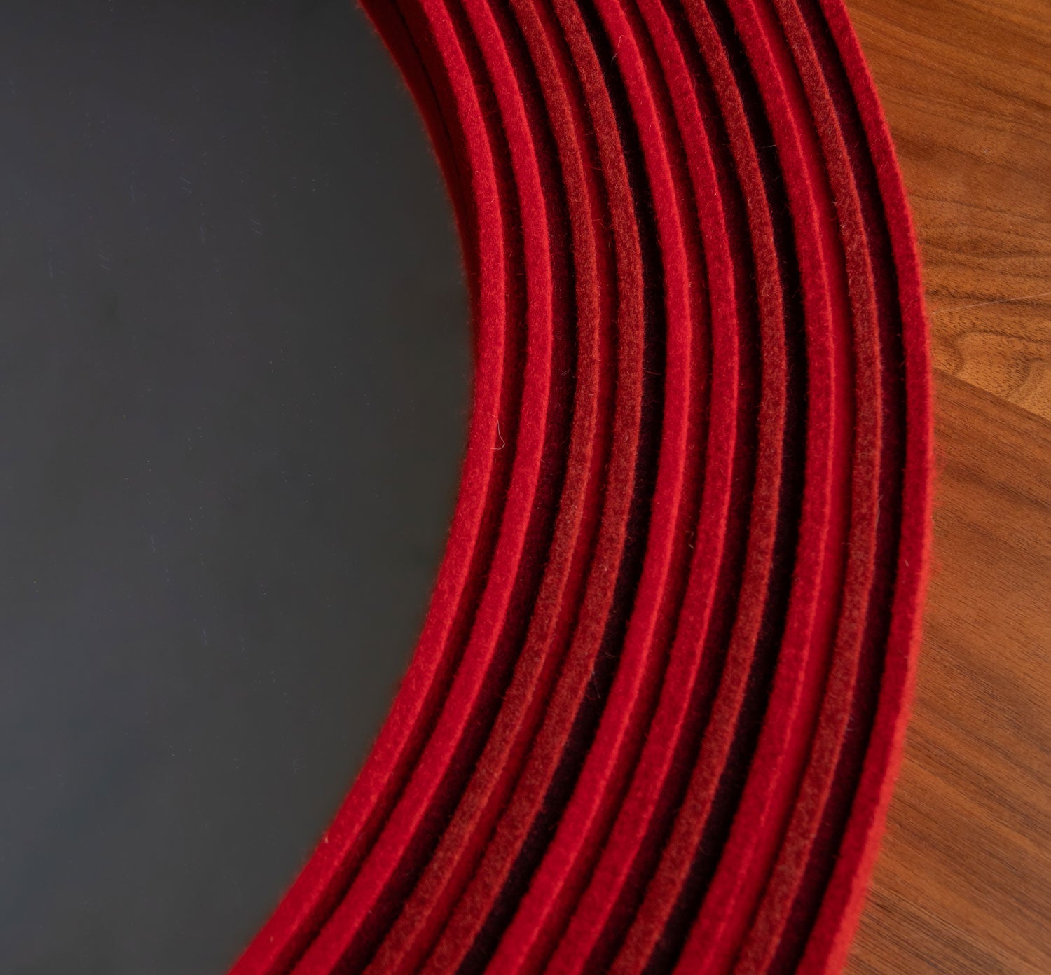 Close up of the felt frame of a mirror. The felt is on edge in alternating heights in tones of red. 