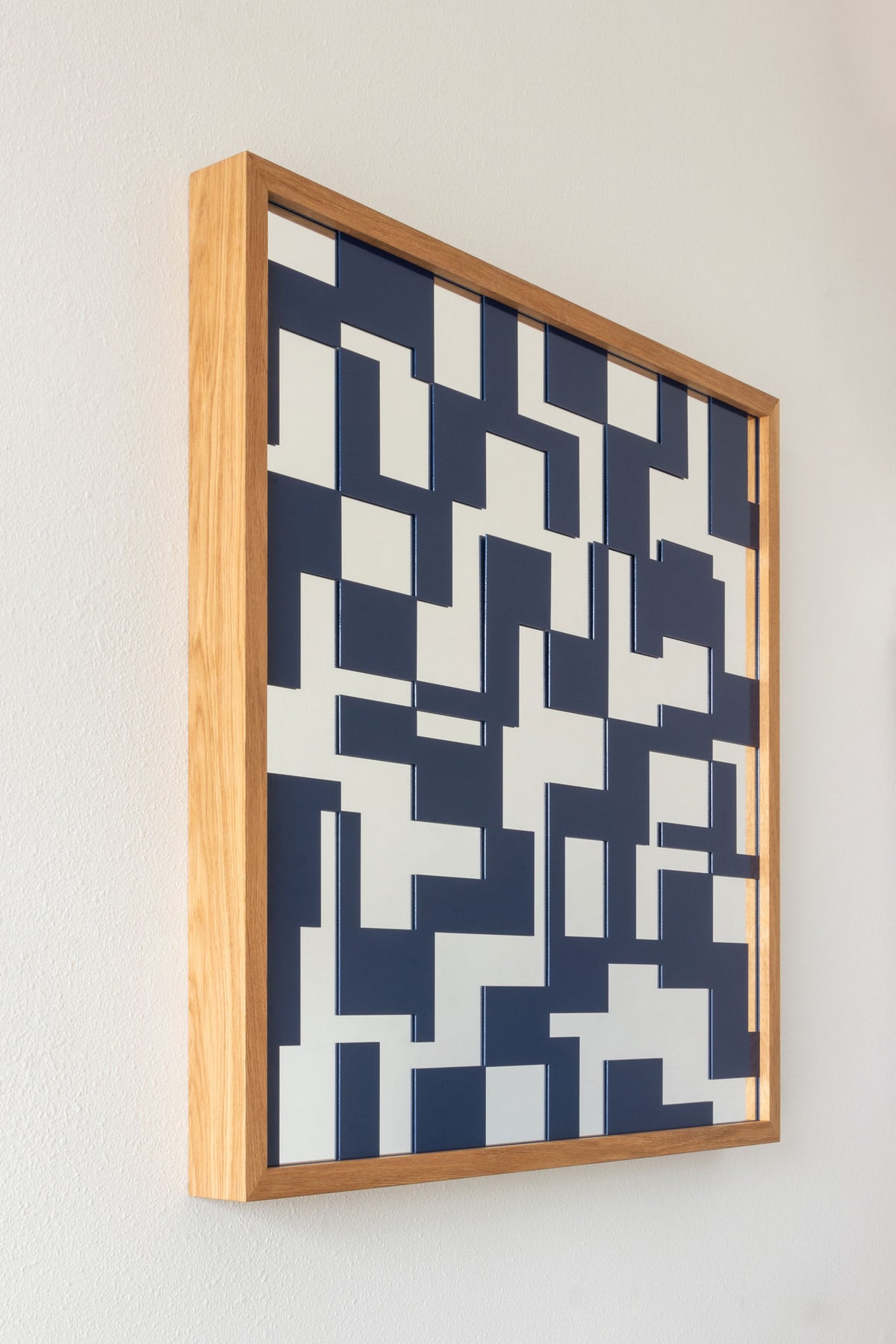 A side angle of a modern geometric mirror featuring a navy blue metal lattice with rectangular shapes over a glass mirror, with a light natural wood frame.