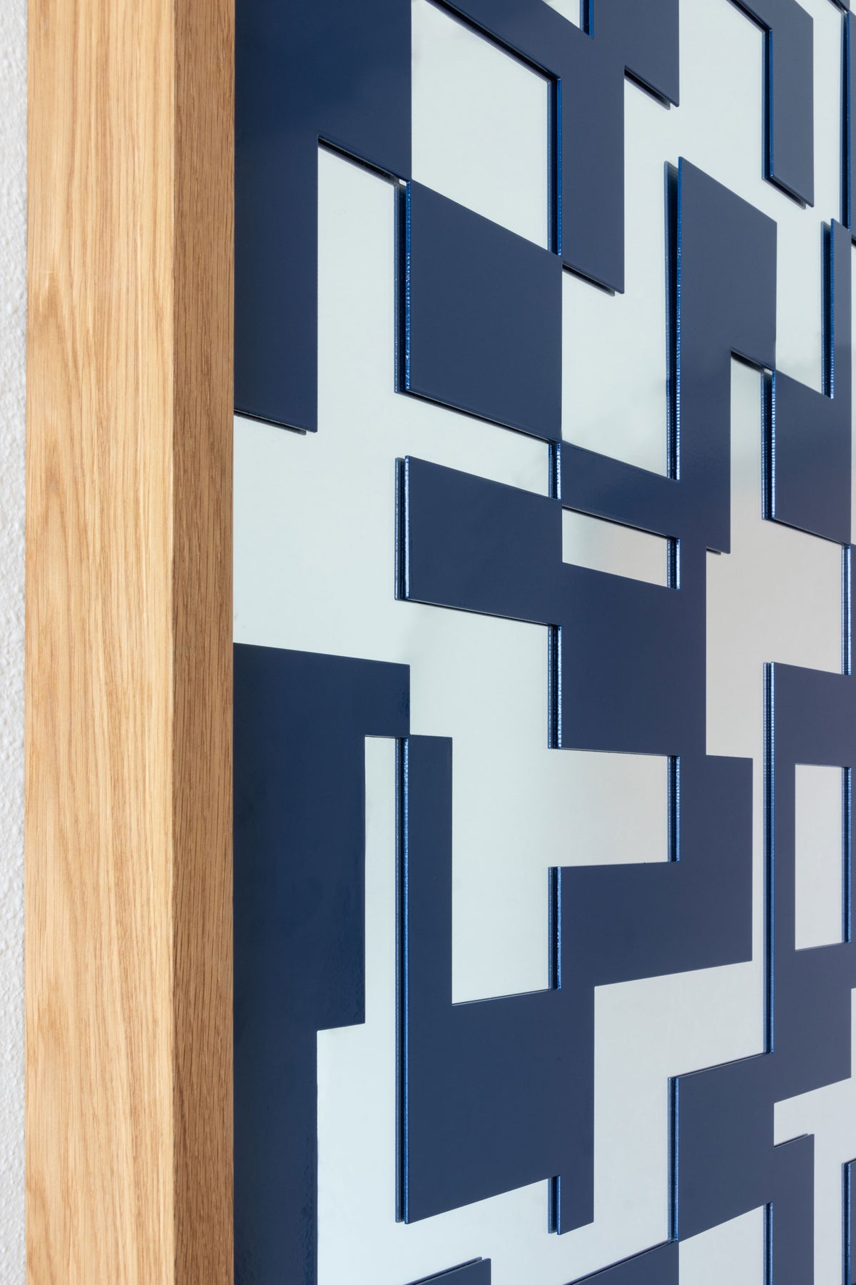 A close-up of a modern geometric mirror featuring a navy blue metal lattice with rectangular shapes over a glass mirror, with a light natural wood frame.