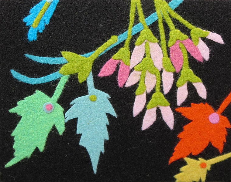 A close-up of a colorful felt embroidery or applique design on a black fabric background, featuring green, light blue, pink, orange, and yellow leaf and flower motifs.