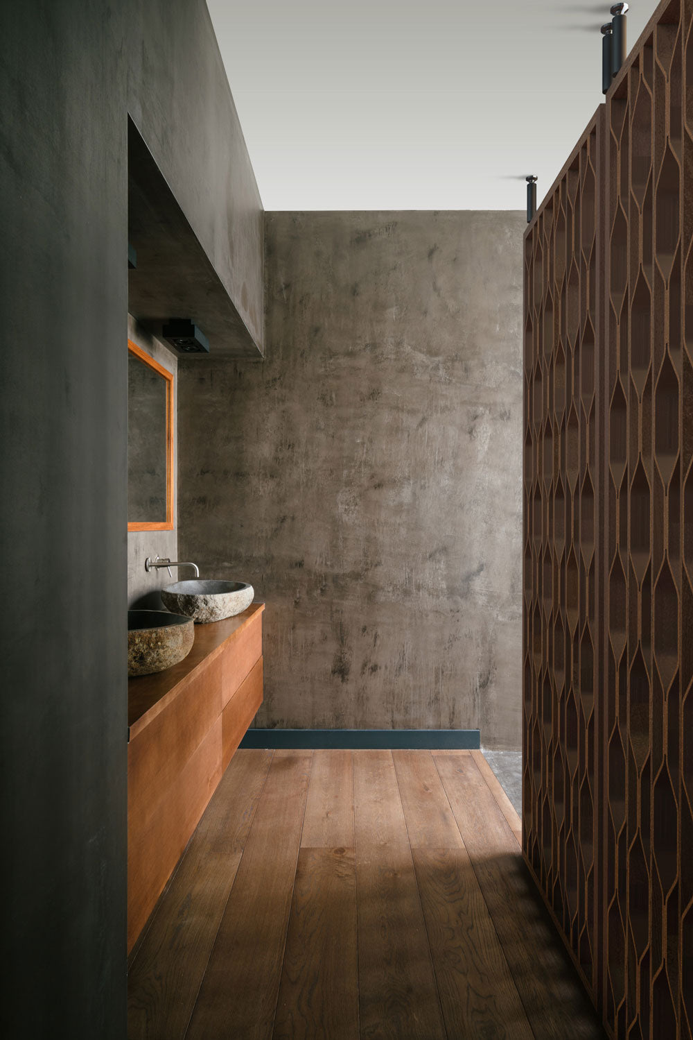 A modern bathroom interior with a concrete wall, wood vanity, stone vessel sink, and a dark brown patterned privacy screen on the right.