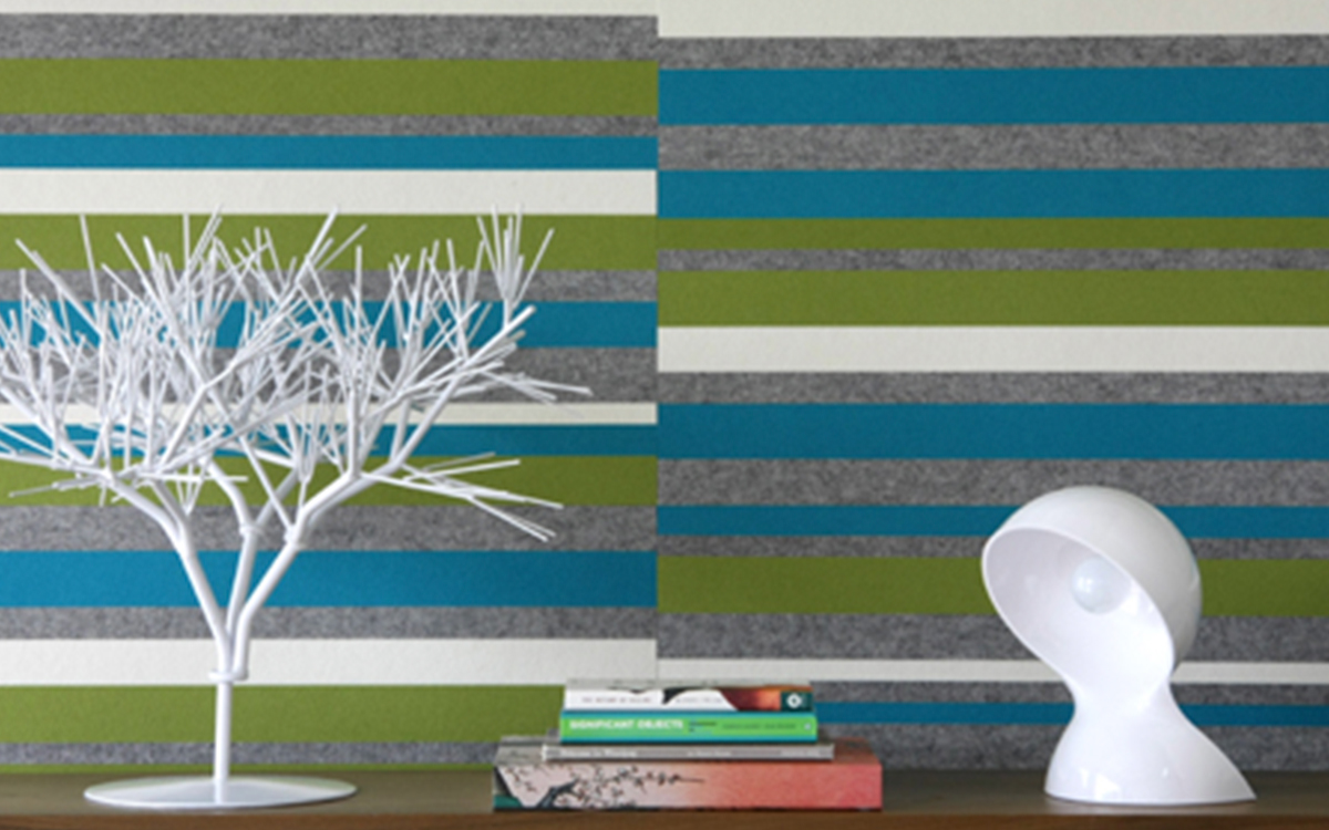 Blue, green, gray and white felt wall with horizontal stripes behind white twig art and a white table lamp