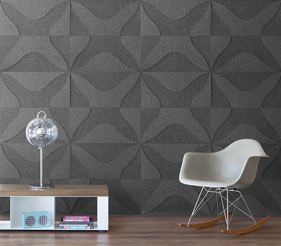 A room scene with a low table and Eames rocking chair. The wall is covered in a two tone gray felt wall covering. The pattern is a thick X