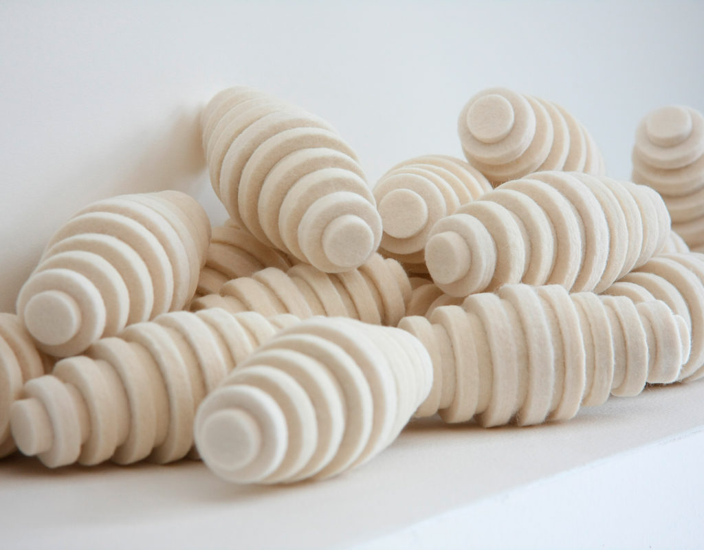 Pile of cream colored felt pods. They are oblong egg-shaped and have ridges.