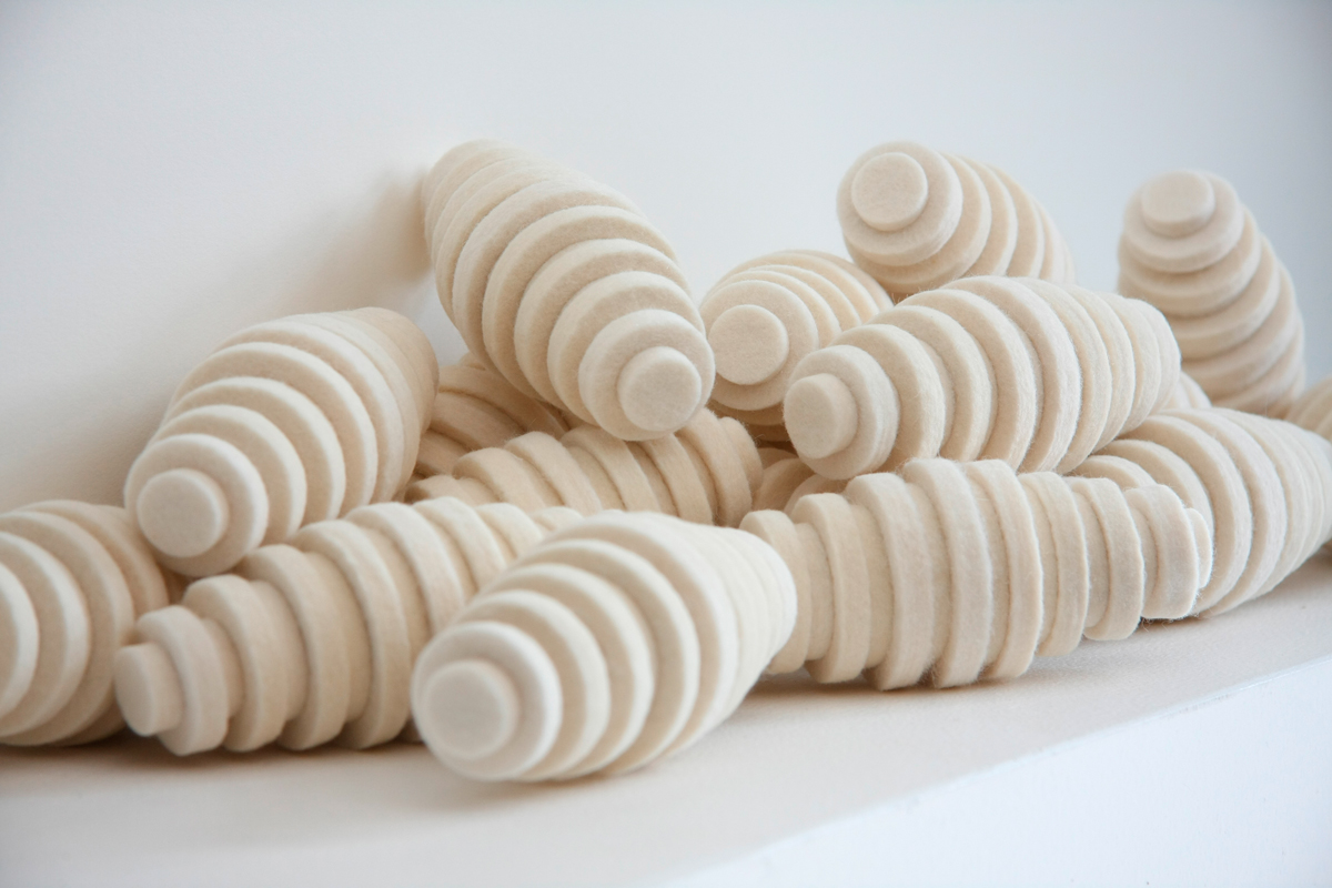 Pile of cream colored felt pods. They are oblong egg-shaped and have ridges.