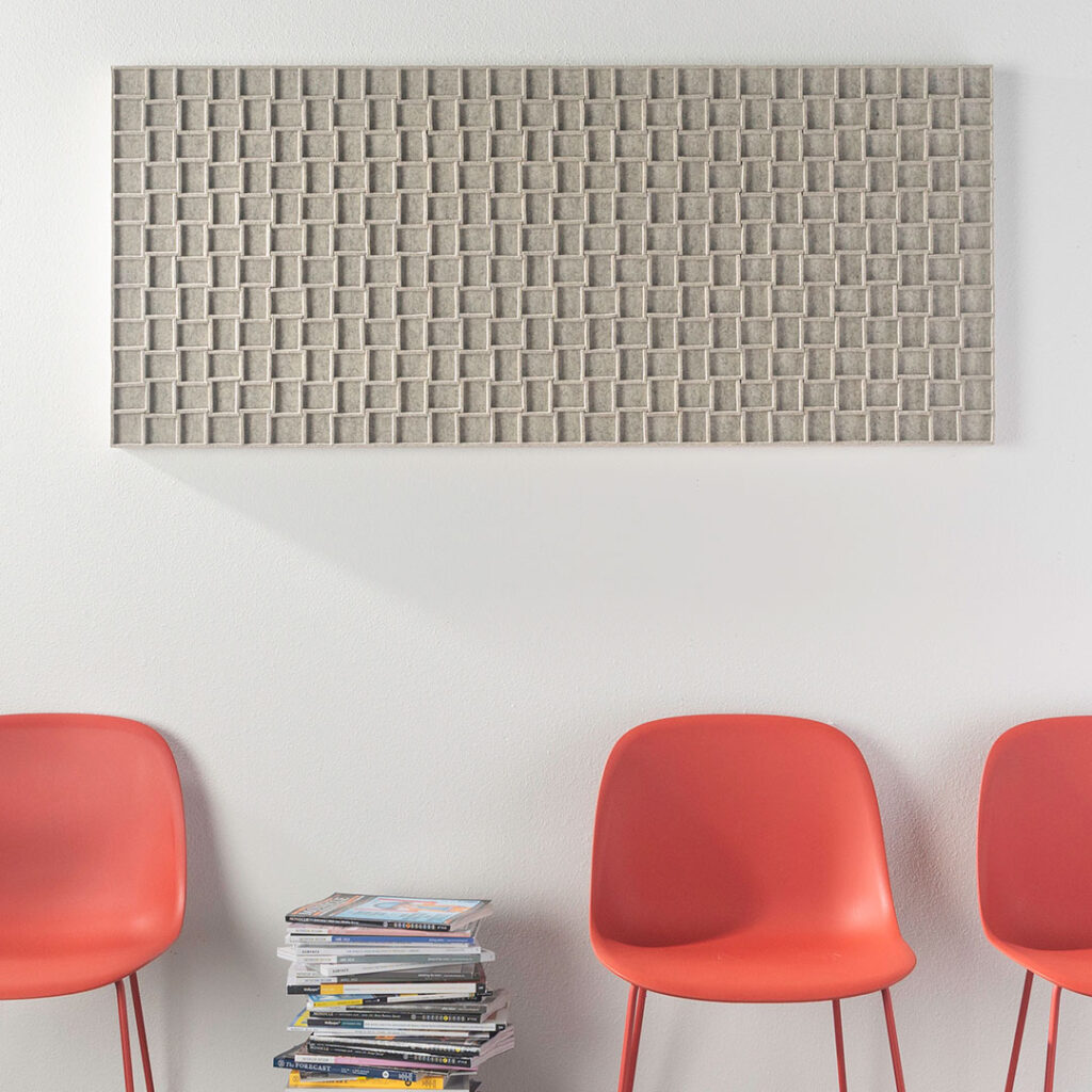 a Submaterial Odessa wall panel made from heathered gray wool felt hangs above red muuto chairs