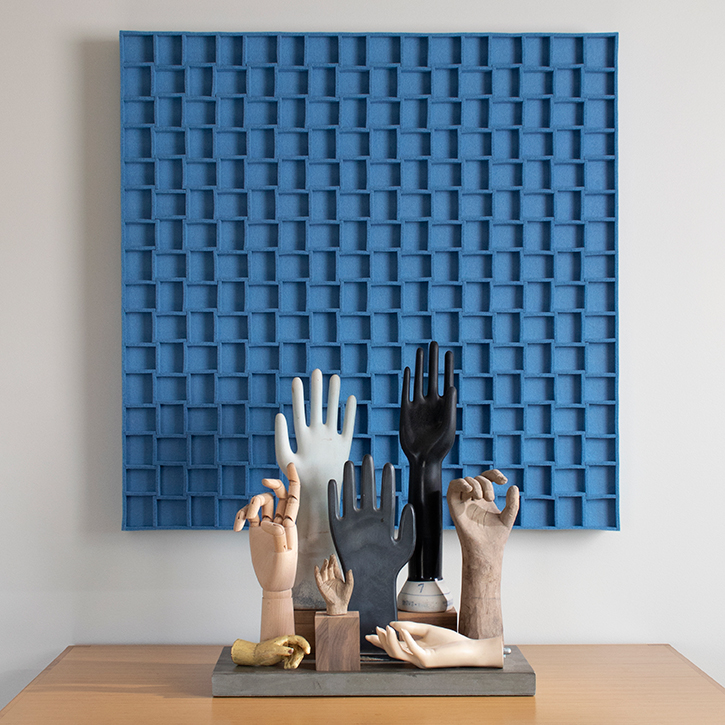 light blue felt submaterial odessa wall decor panel hanging behind a collection of sculptural hands