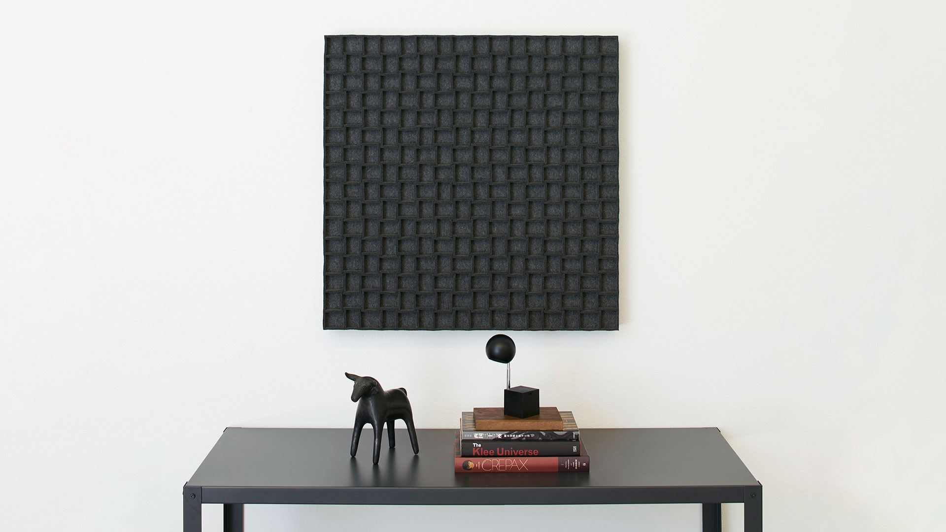 a charcoal grey Submaterial wall art panel made from wool felt hangs above a sidetable