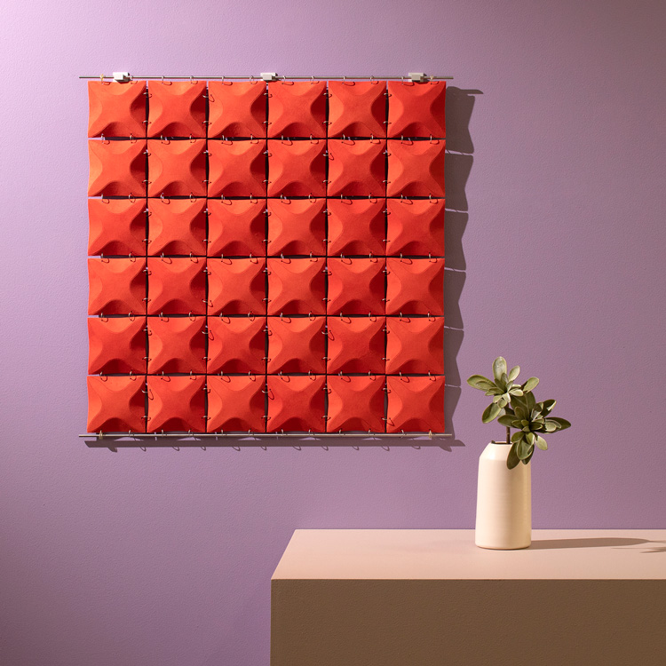 A square bright red-orange dimensional wall hanging on a lavender wall