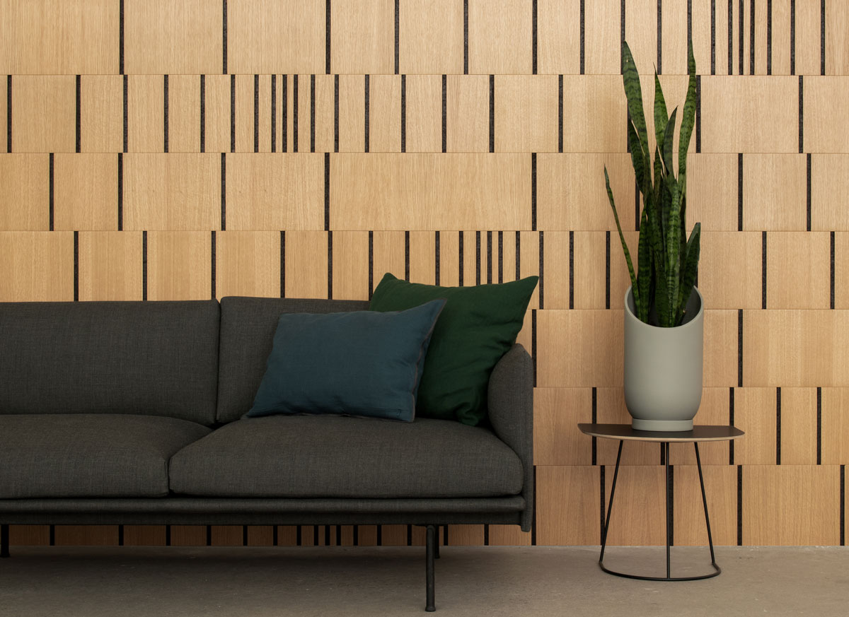 Wood wall covering in white oak and smoked cork with varying concentrations of vertical lines at random intervals. A gray couch and table with a snake plant are in front of the wall