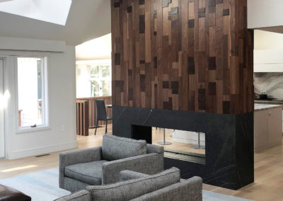 A living room with a freestanding fireplace covered to the ceiling with different sized walnut wood pieces