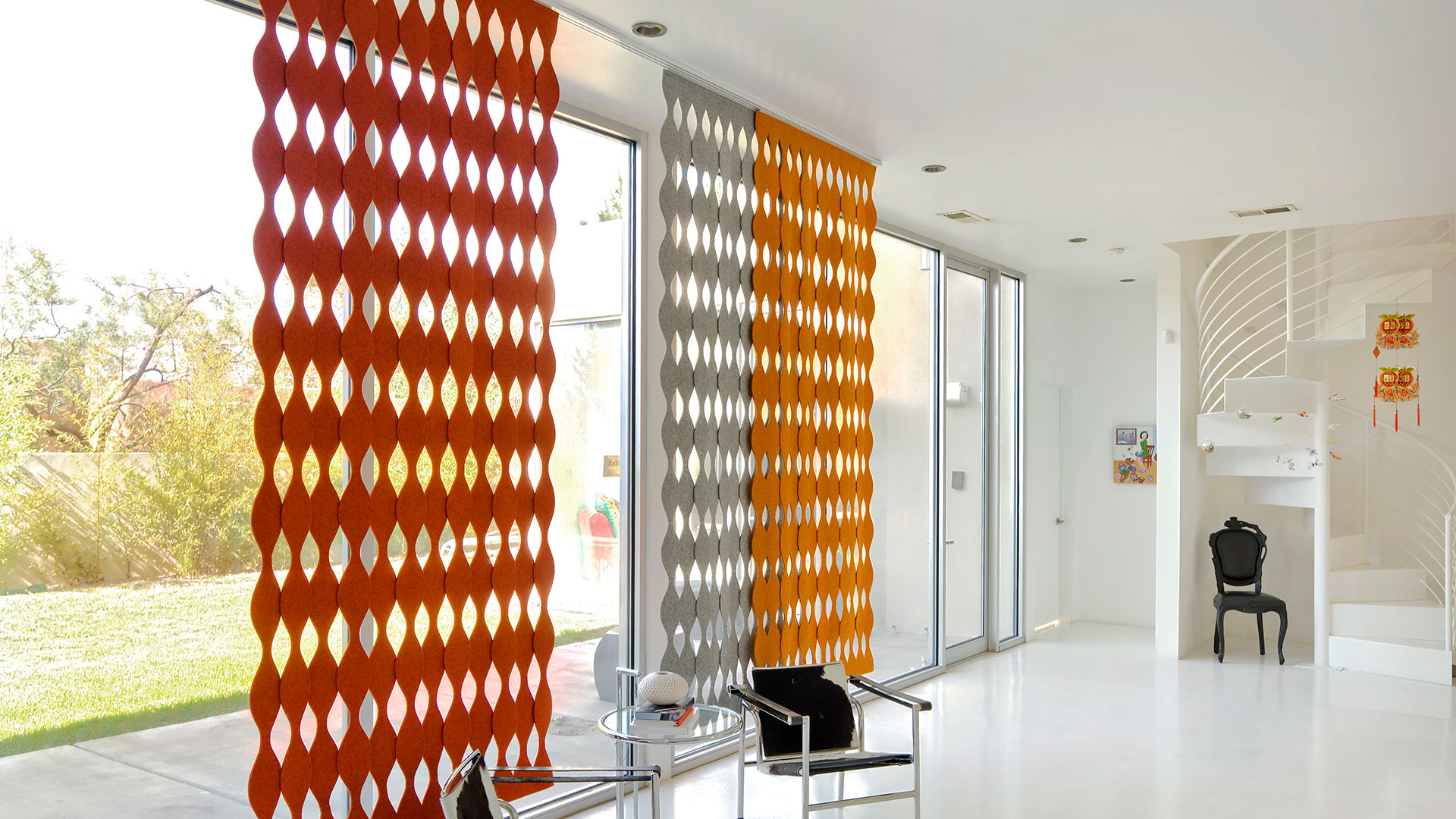 Red, gray and orange wavy felt screens cover a floor to ceiling window in an all-white home